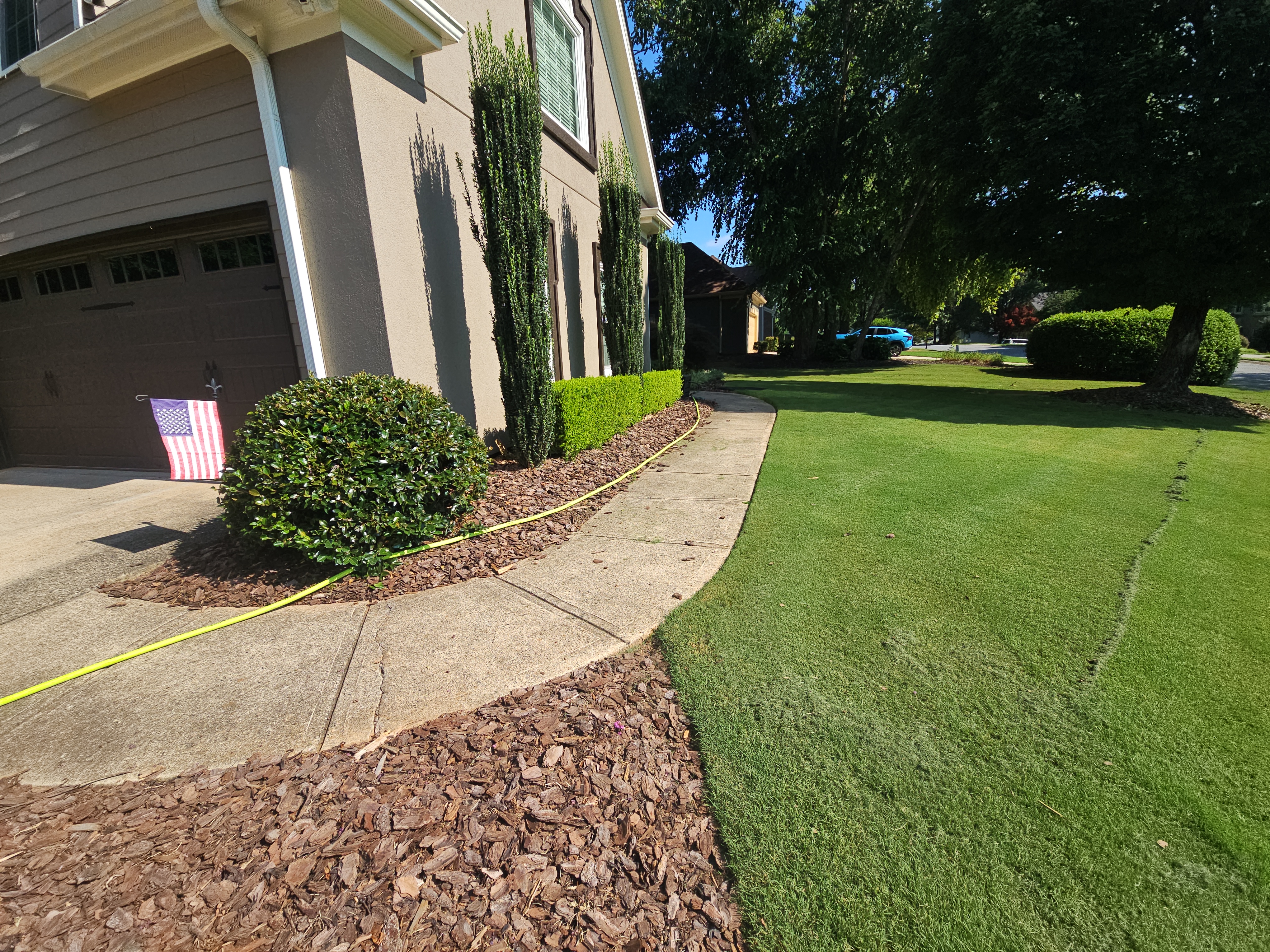 Side concrete walkway along the garage of a residential home in Alpharetta, GA, with pressure washing hose laid out.