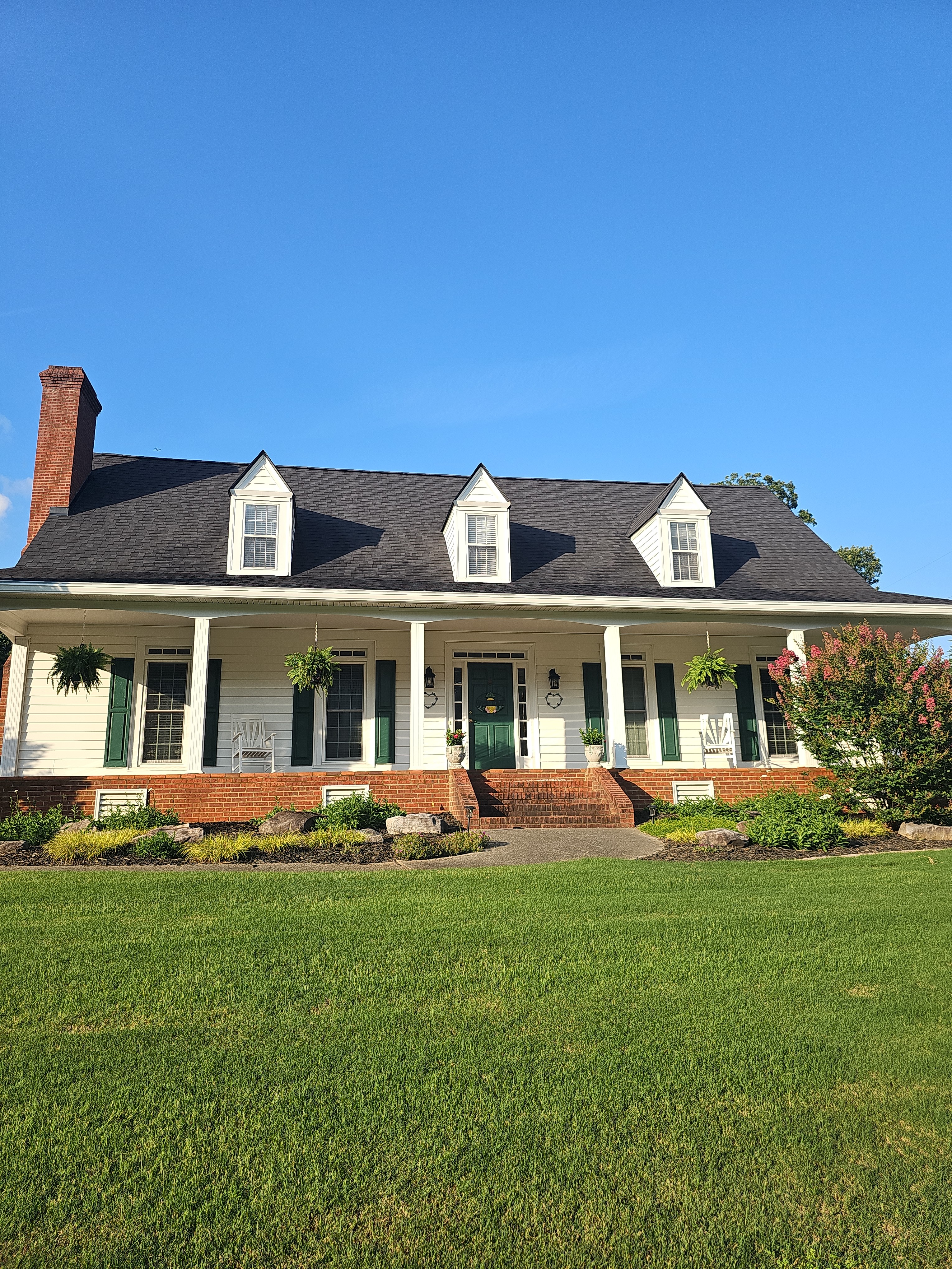 Full front view of a large white house with a wraparound covered porch, green shutters, and a brick foundation after a house wash in Kennesaw, GA.