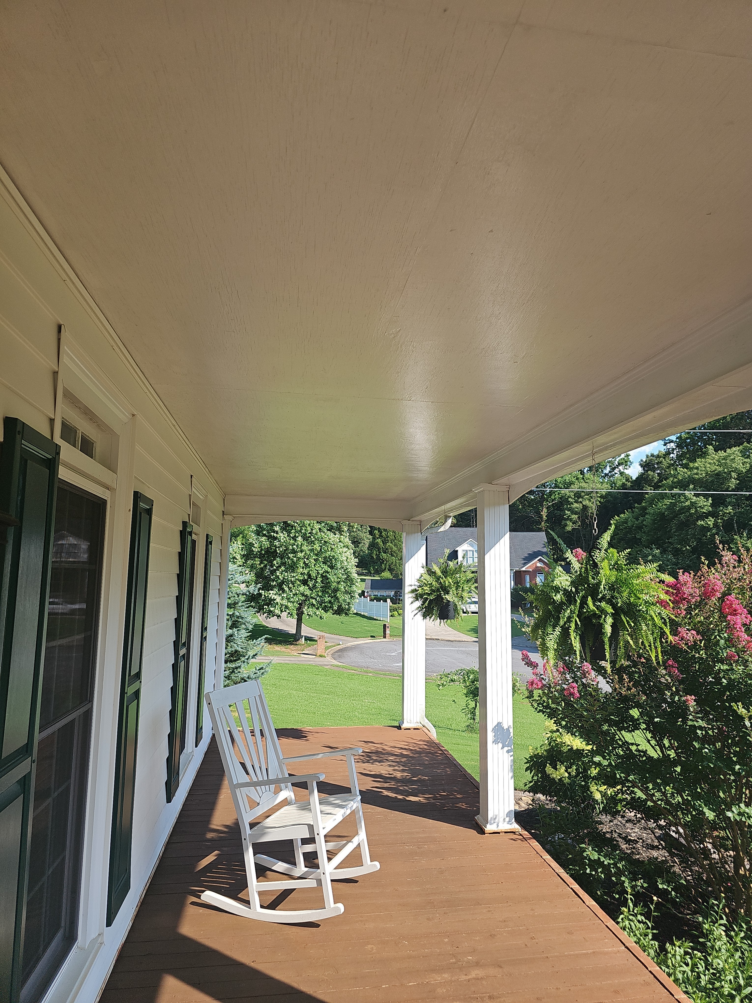 Interior of a covered front porch with wood deck flooring, white columns, and a rocking chair at a Kennesaw, GA home.