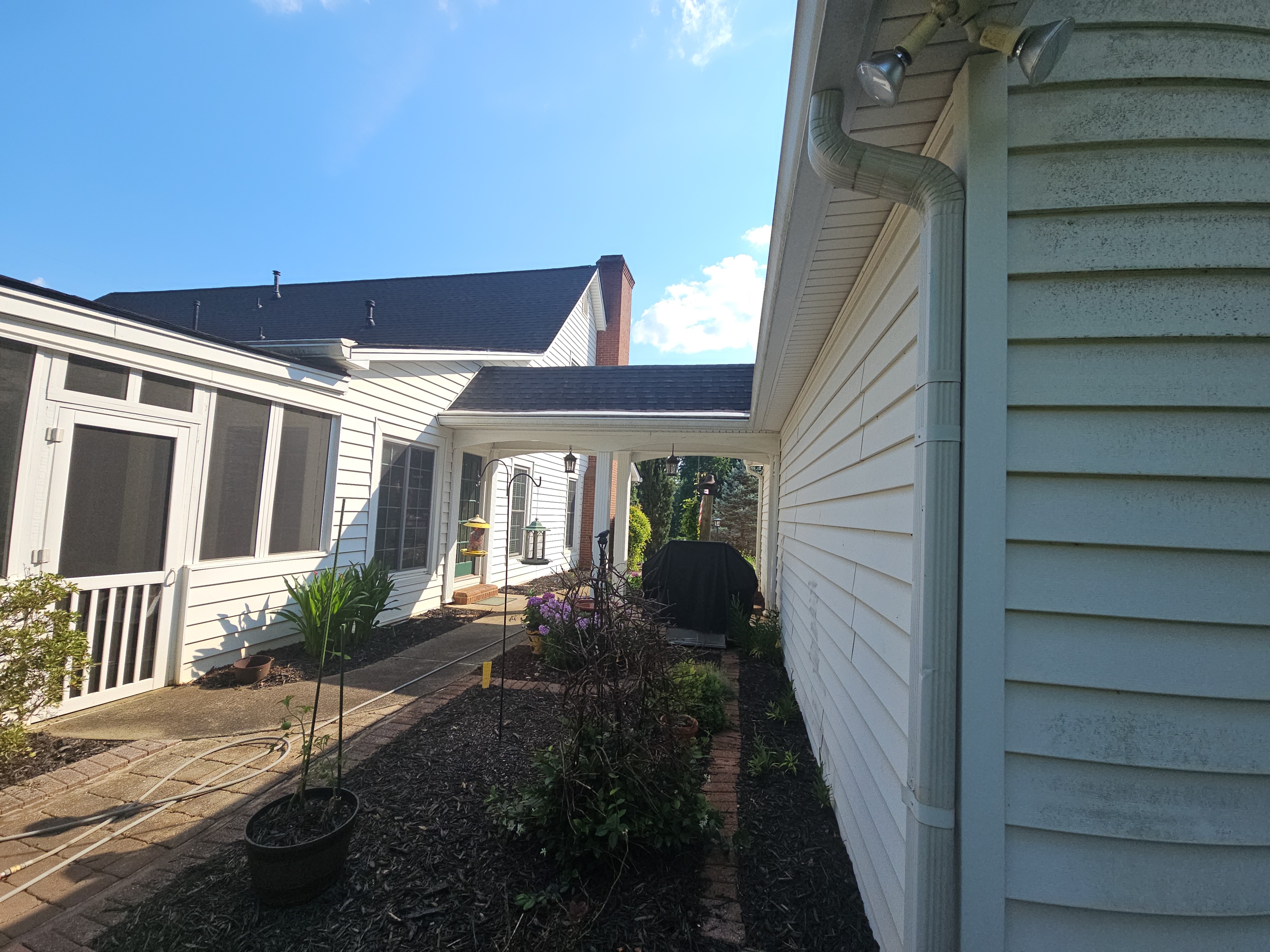 Side of a home showing vinyl siding, a downspout with visible streaking, and the screened porch addition in the background, before a house wash in Kennesaw, GA.