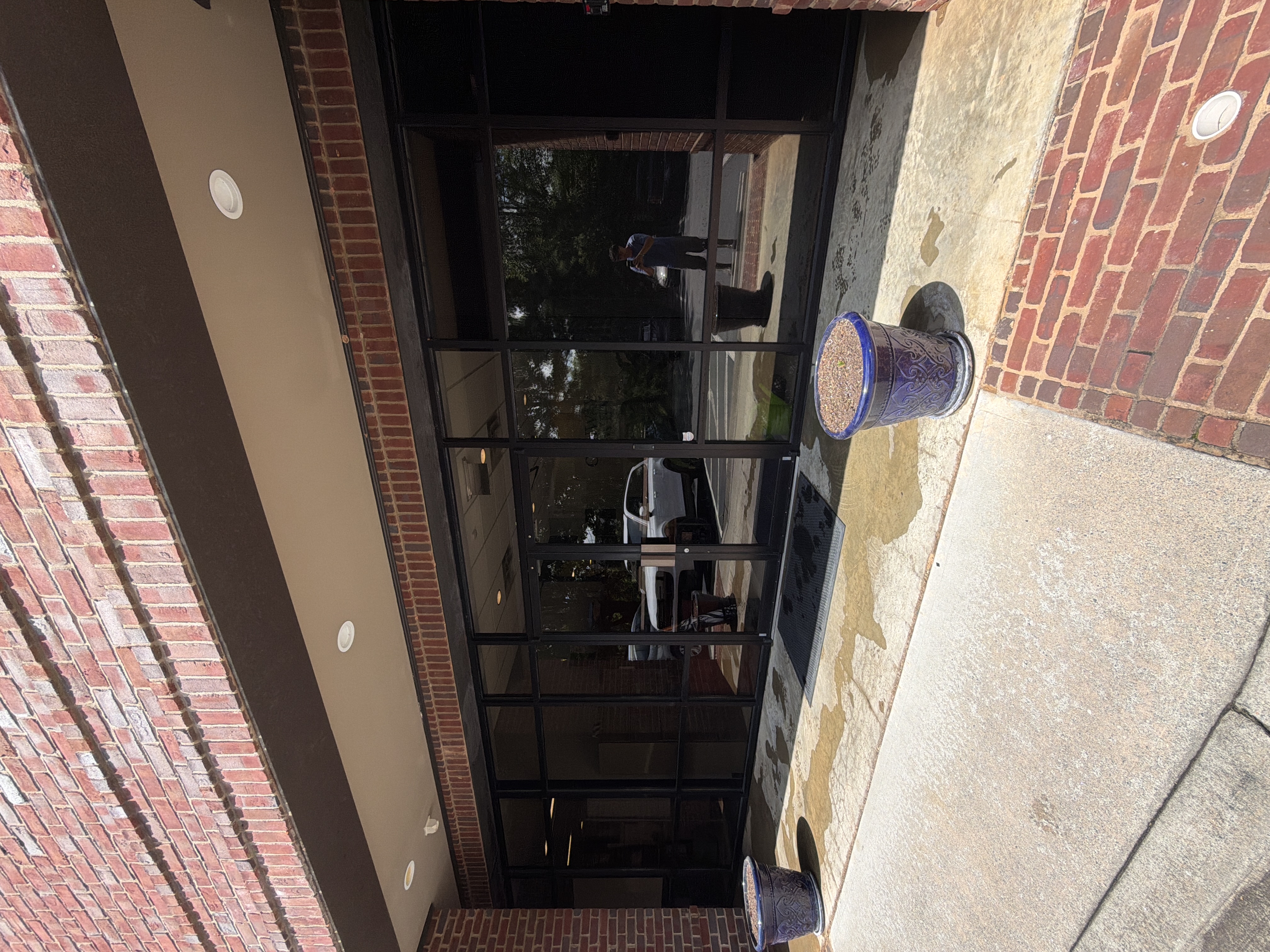 Commercial building front entrance and concrete apron during pressure washing in Alpharetta, GA, with wet pavement, glass storefront, and potted planters visible