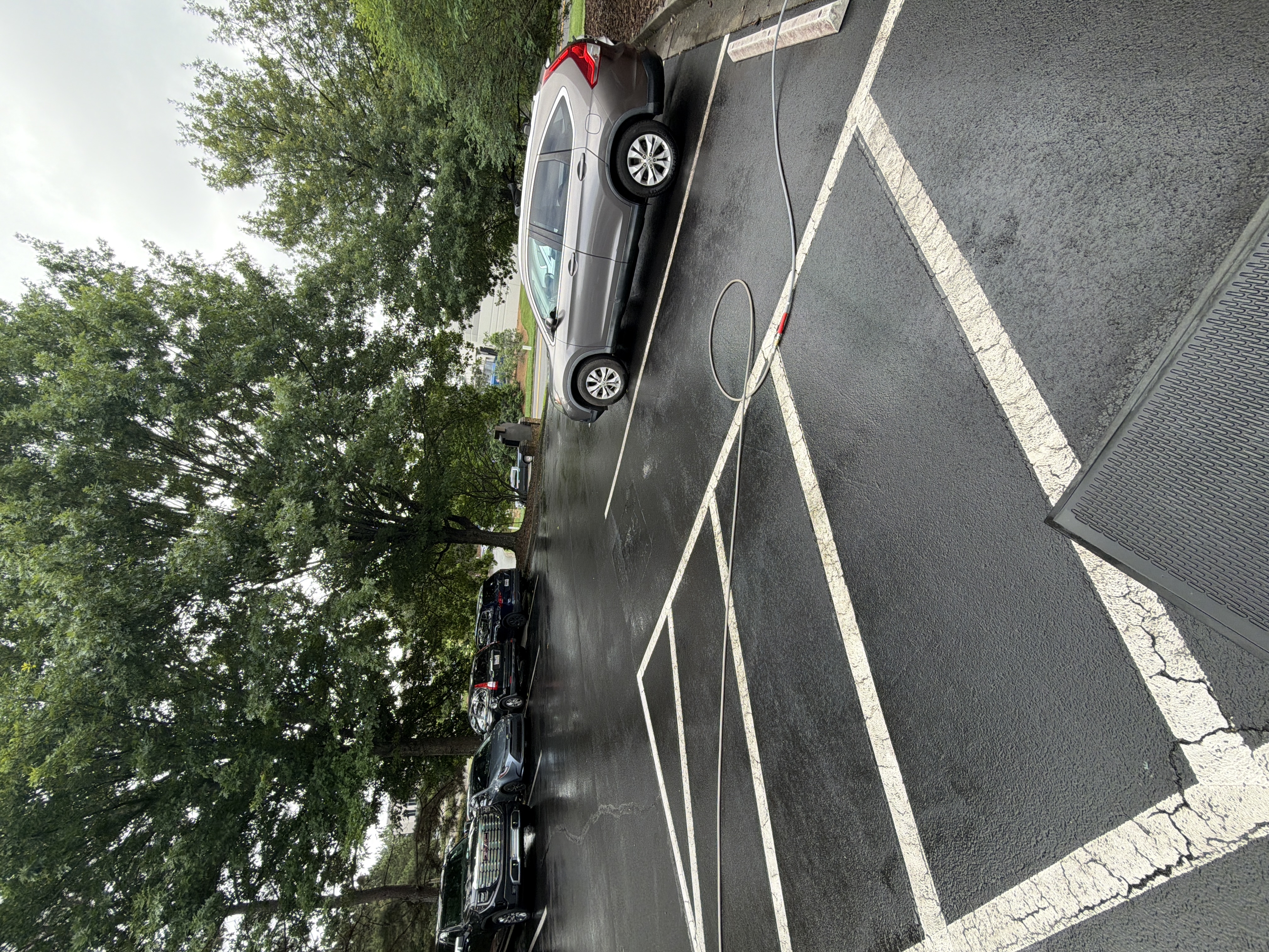 Asphalt parking lot being pressure washed in Alpharetta, GA, with pressure hose laid across wet pavement and parking stall lines visible