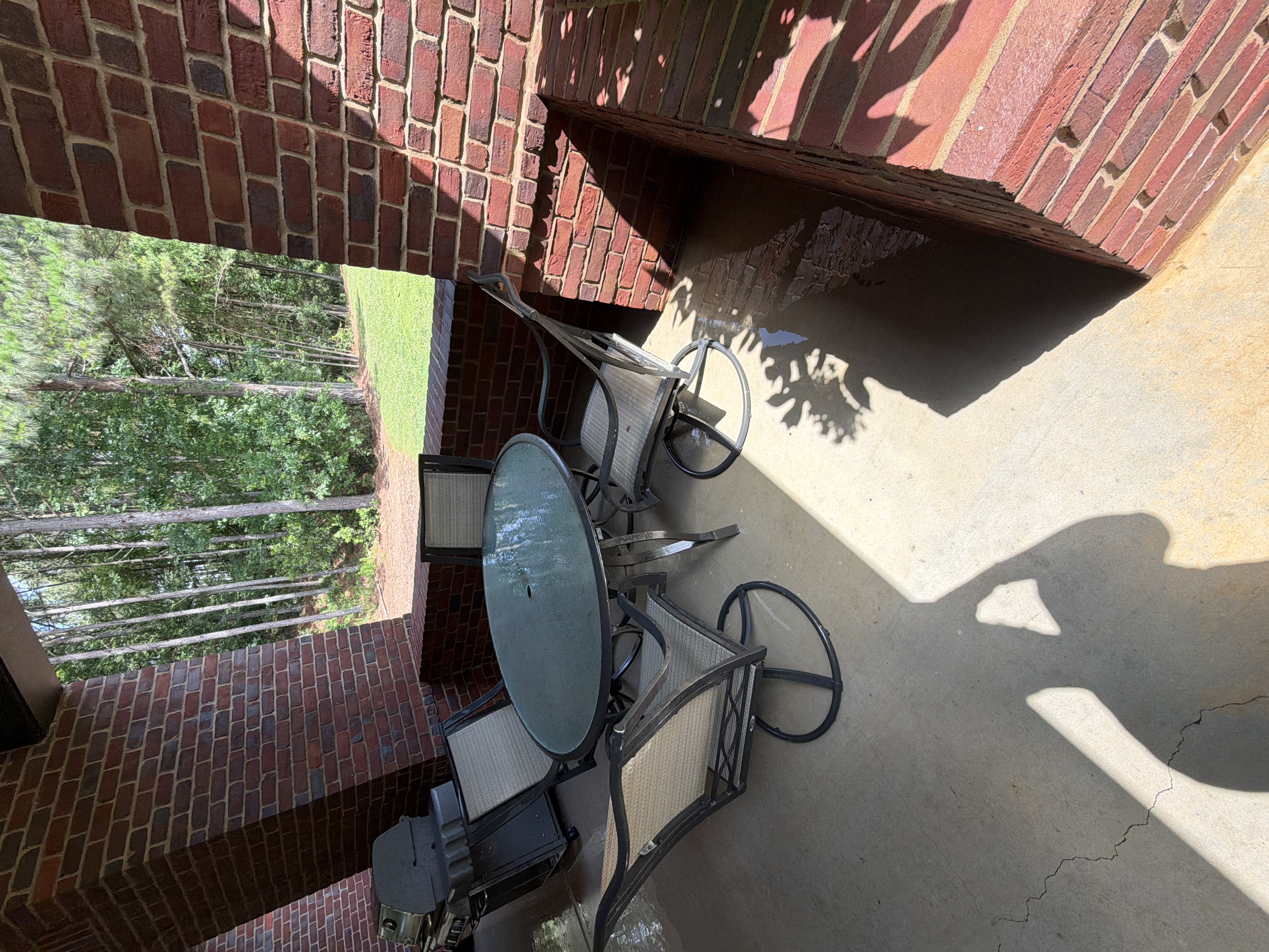 Clean covered concrete patio after pressure washing in Alpharetta, GA, with outdoor dining set, brick columns, and a gas grill visible in natural light