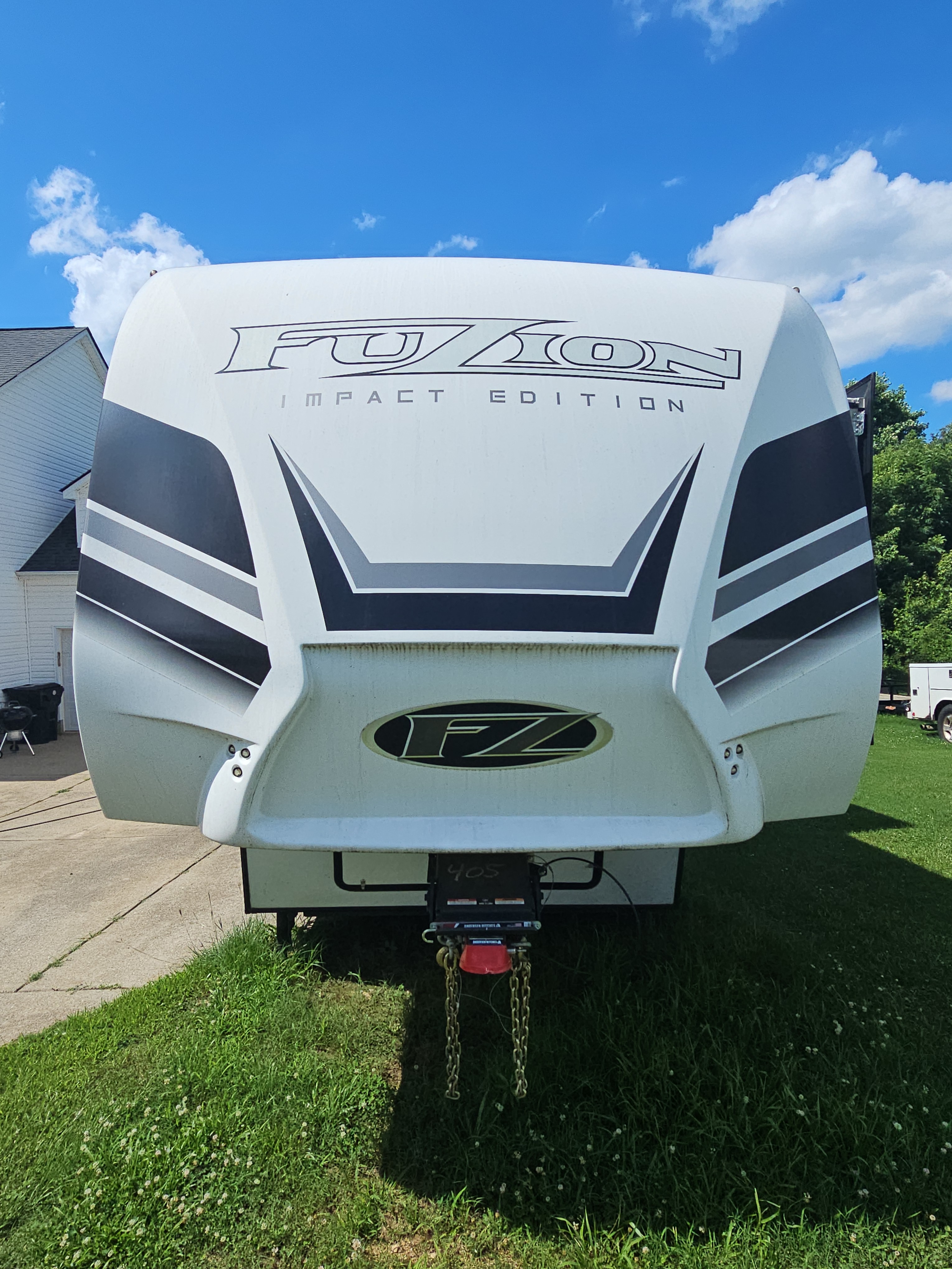 Front nose of a white Fuzion Impact Edition fifth-wheel RV parked on grass at a Canton, GA property.
