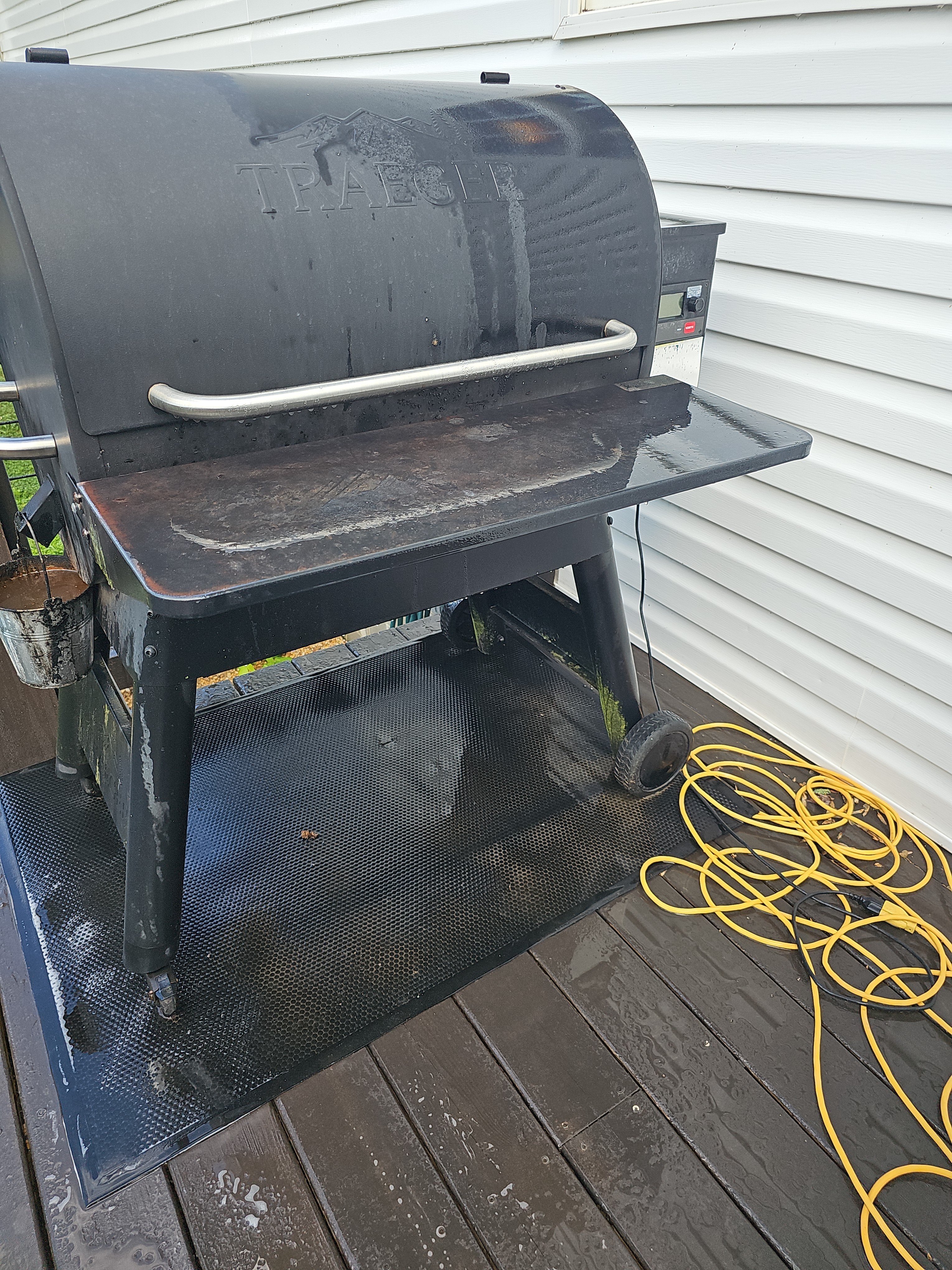 Wet wood deck with a Traeger pellet grill and pressure washing hose visible during a house wash in Canton, GA.