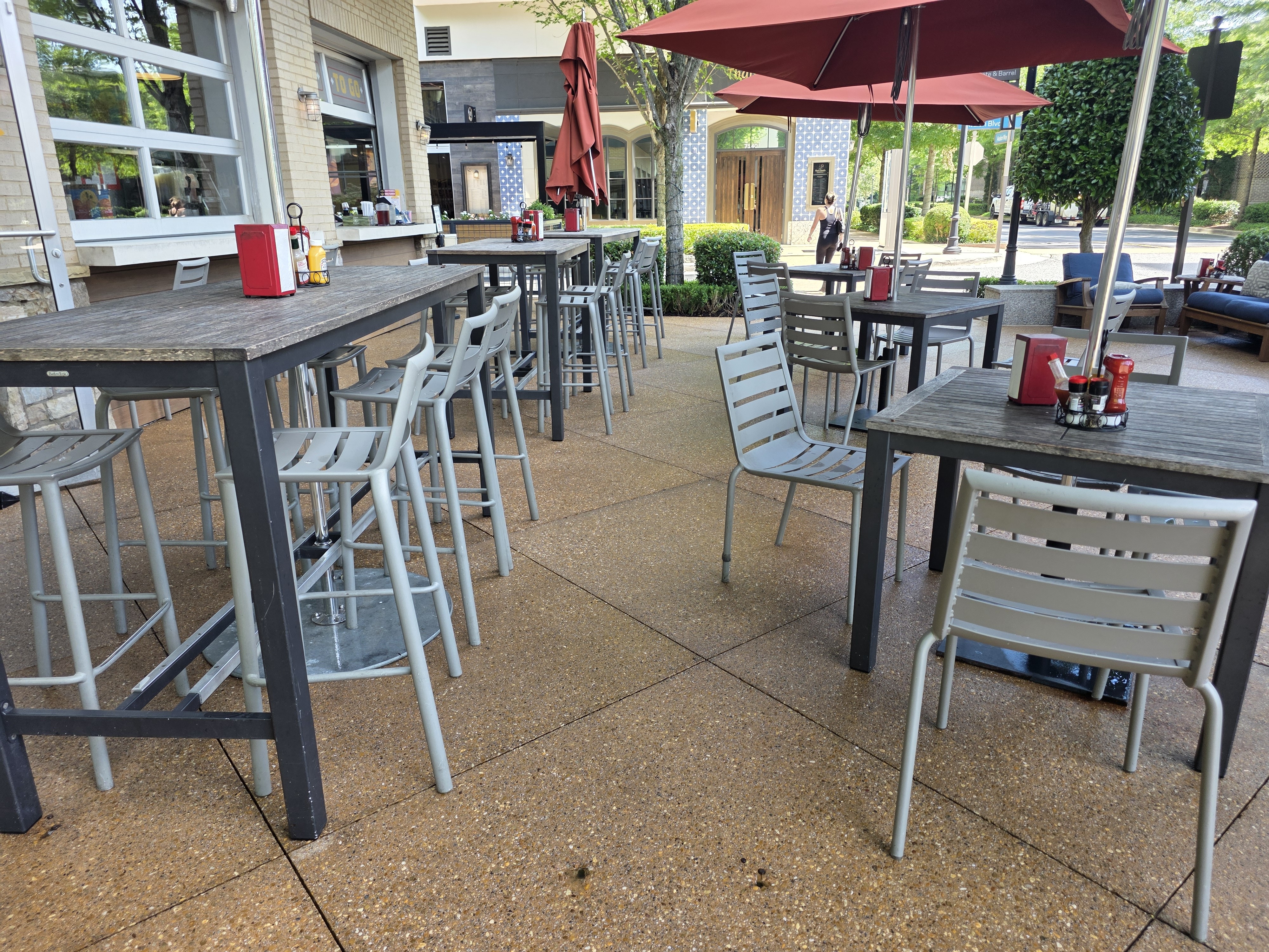 Exposed-aggregate concrete patio with dining tables and red umbrellas at a commercial degreasing job in Alpharetta, GA.