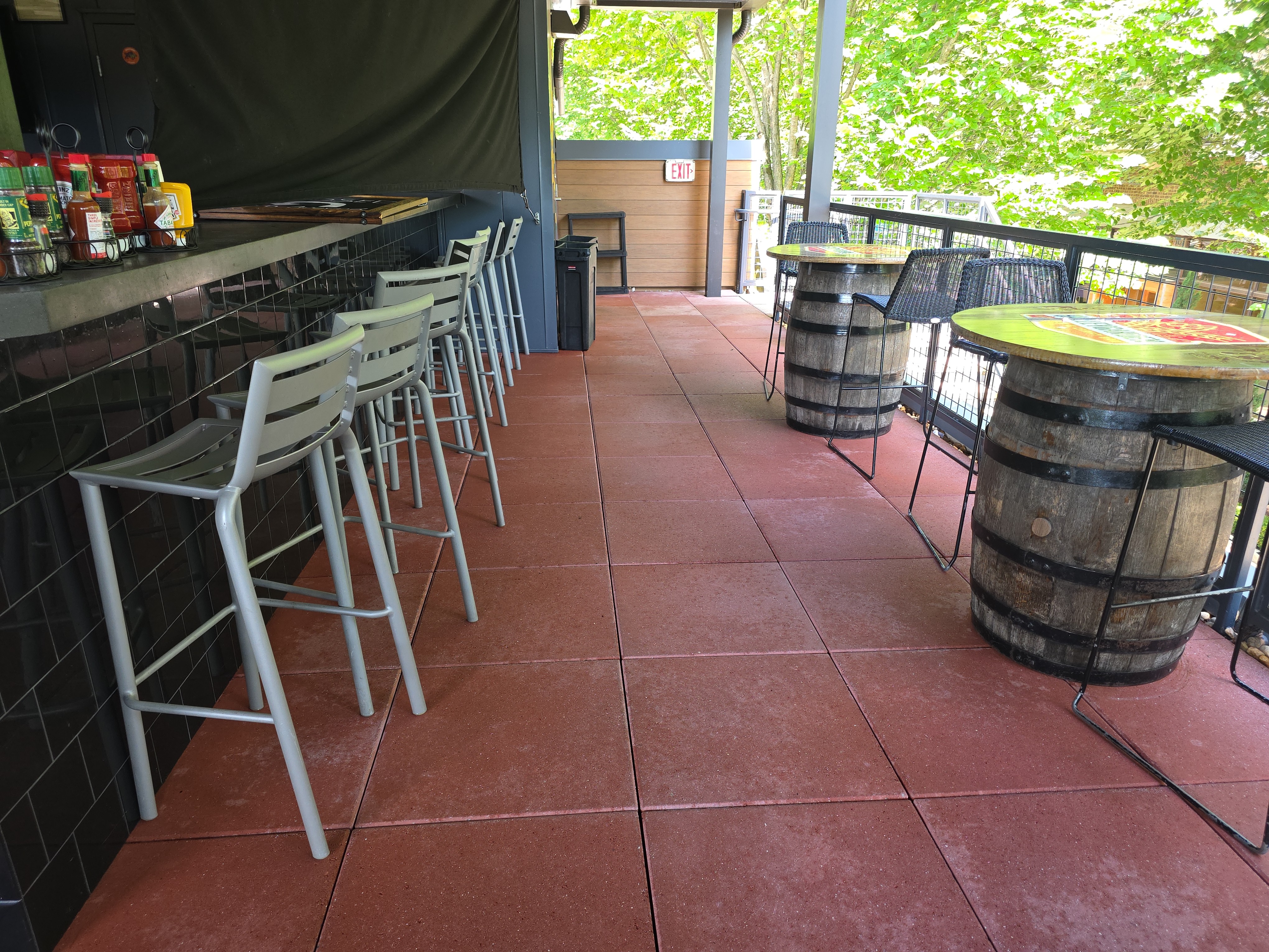 Red-tinted concrete tile floor on a covered rooftop bar patio with barrel tables at a commercial degreasing job in Alpharetta, GA.