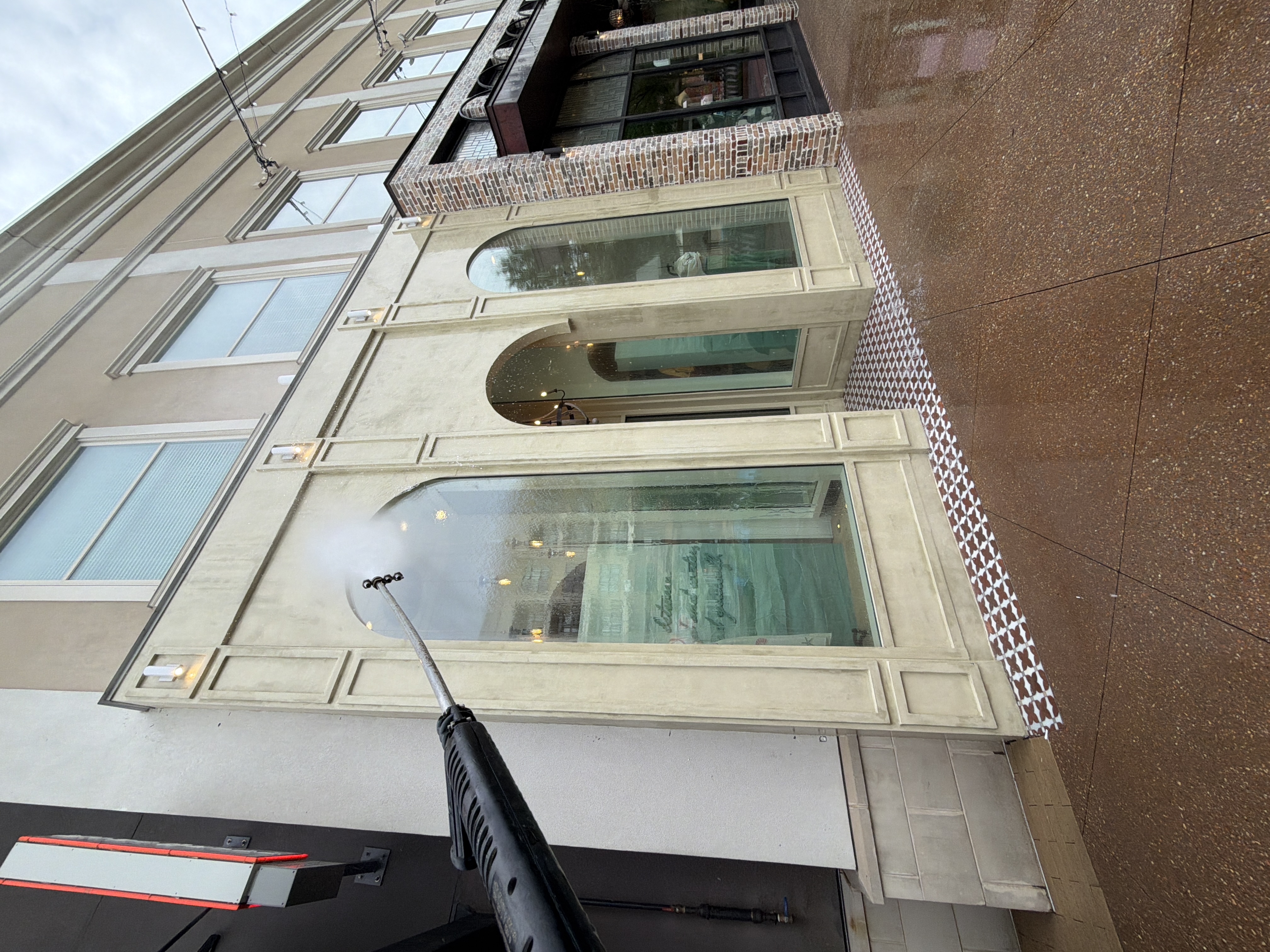 Pressure washing wand cleaning commercial stucco building facade and arched windows in Alpharetta, GA