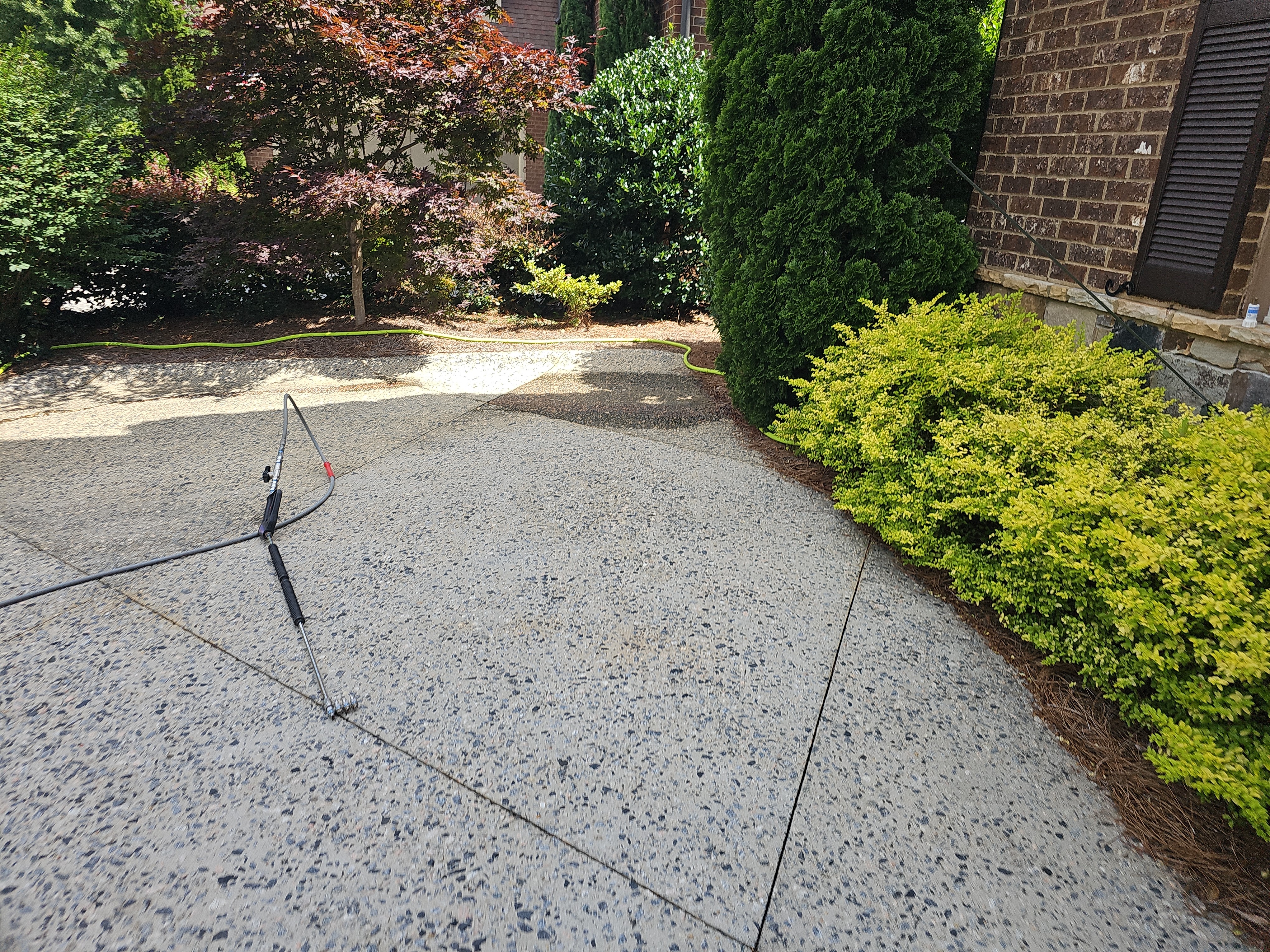 Surface cleaner tool on an exposed aggregate concrete driveway with pressure washing hose in Marietta, GA.