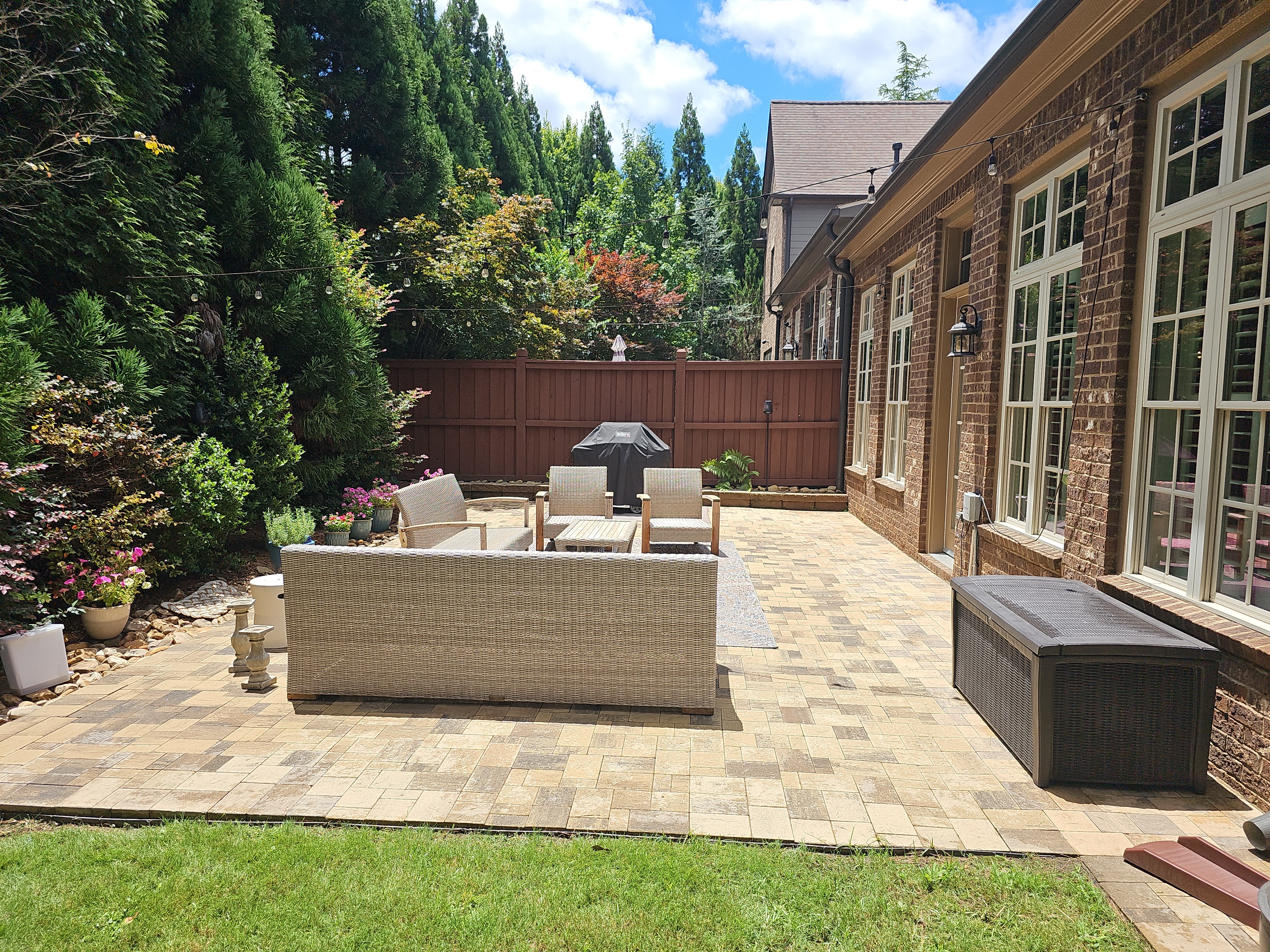 Wide view of a brick paver backyard patio with wicker furniture and wood fence at a home in Marietta, GA.