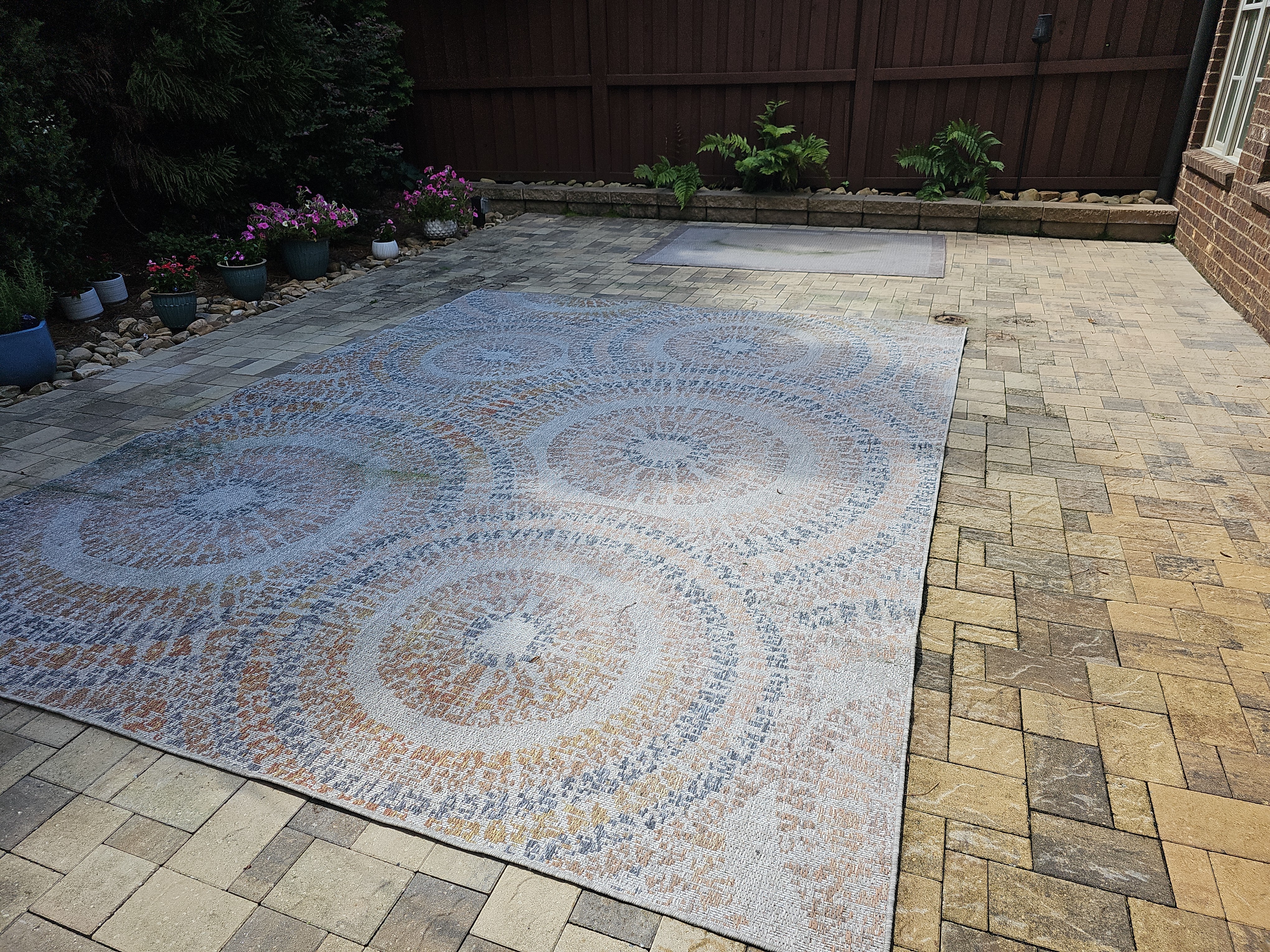 Stone paver patio with an outdoor rug, potted flowers, and wood fence at a pressure washing job in Marietta, GA.