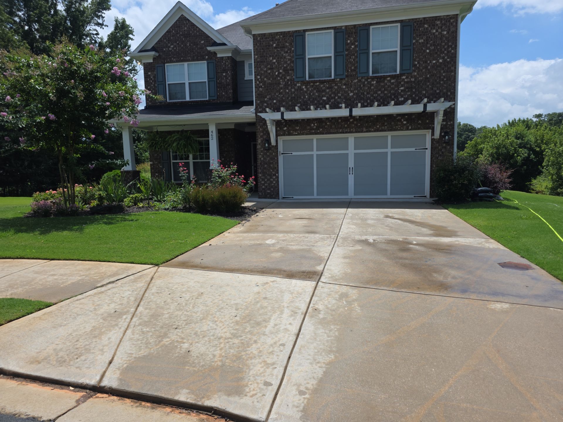 Wide-angle view of a concrete driveway at a two-story brick home in Canton, GA, with staining and discoloration visible on the surface.
