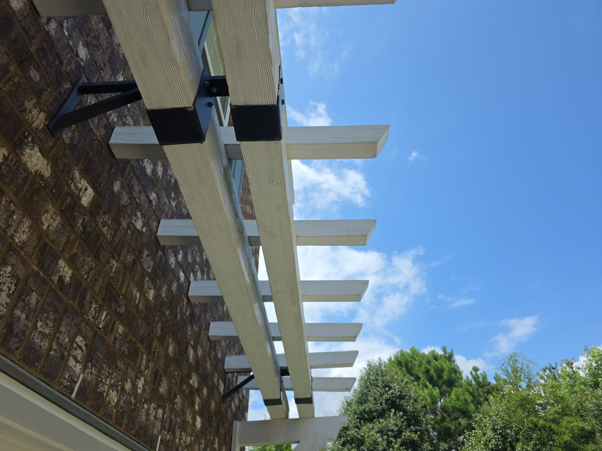 Low-angle view of a white wood pergola attached to a brick home at a pressure washing job in Canton, GA.