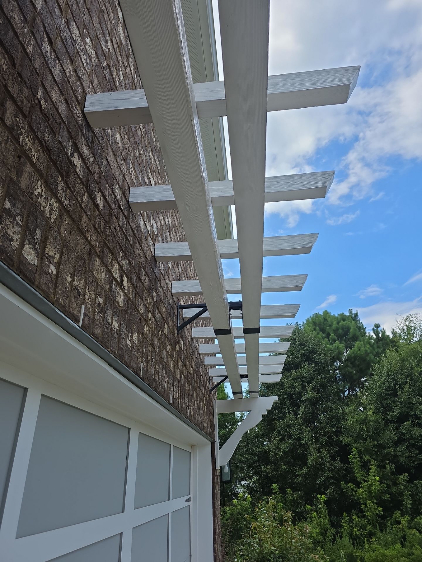 Underside of a white wood pergola attached to a brick wall at a pressure washing job in Canton, GA.