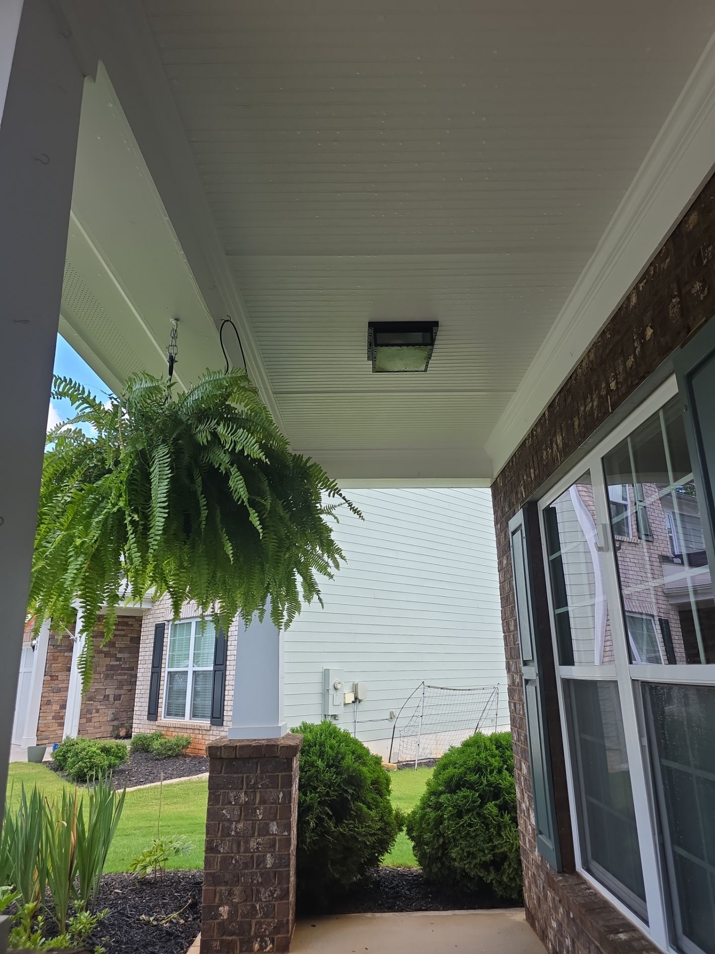 Front porch beadboard ceiling with hanging fern basket and brick columns at a house washing job in Canton, GA.
