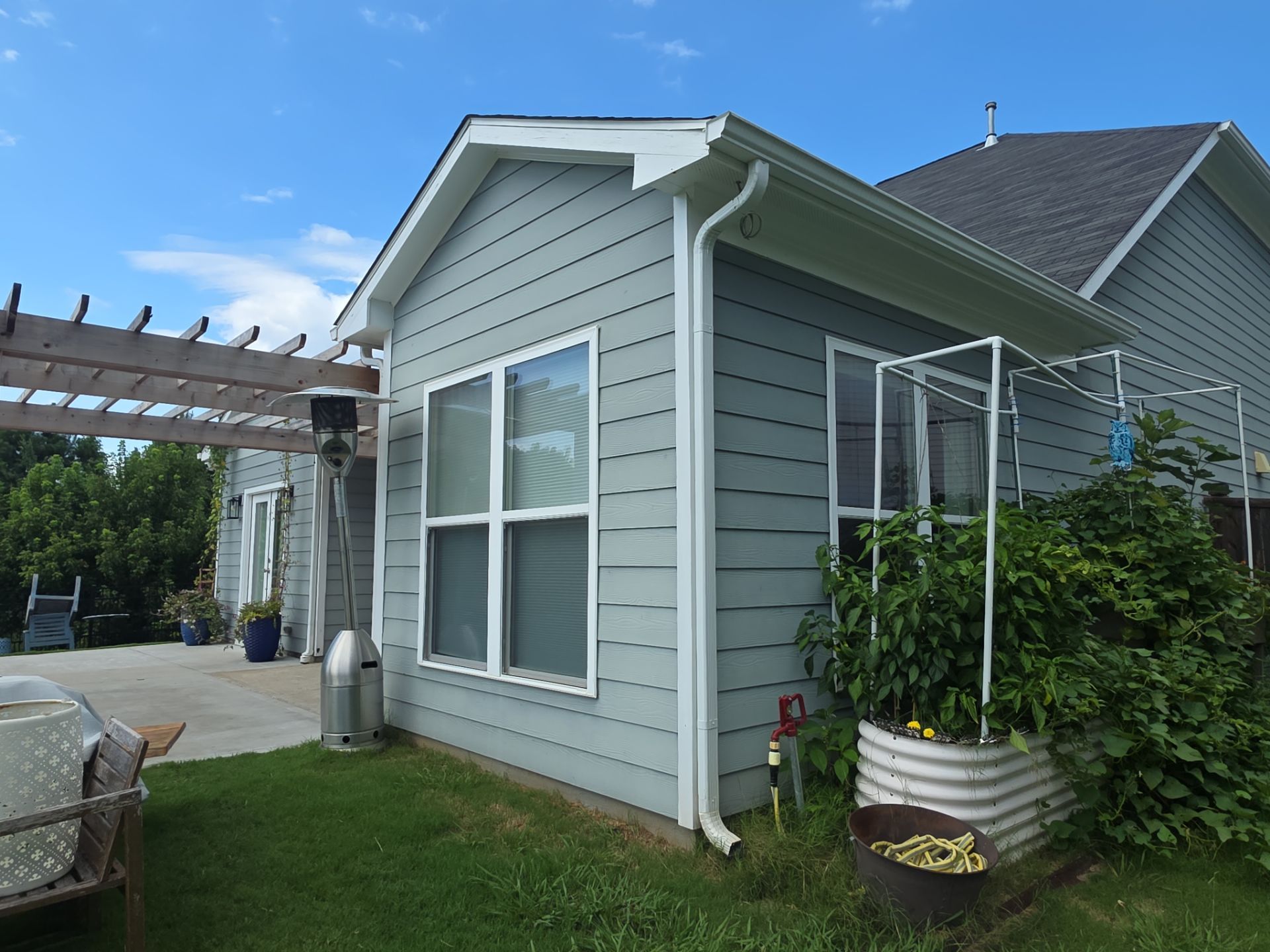 Rear corner of a gray vinyl-sided home with white gutters and a raised garden tub at a house washing job in Canton, GA.