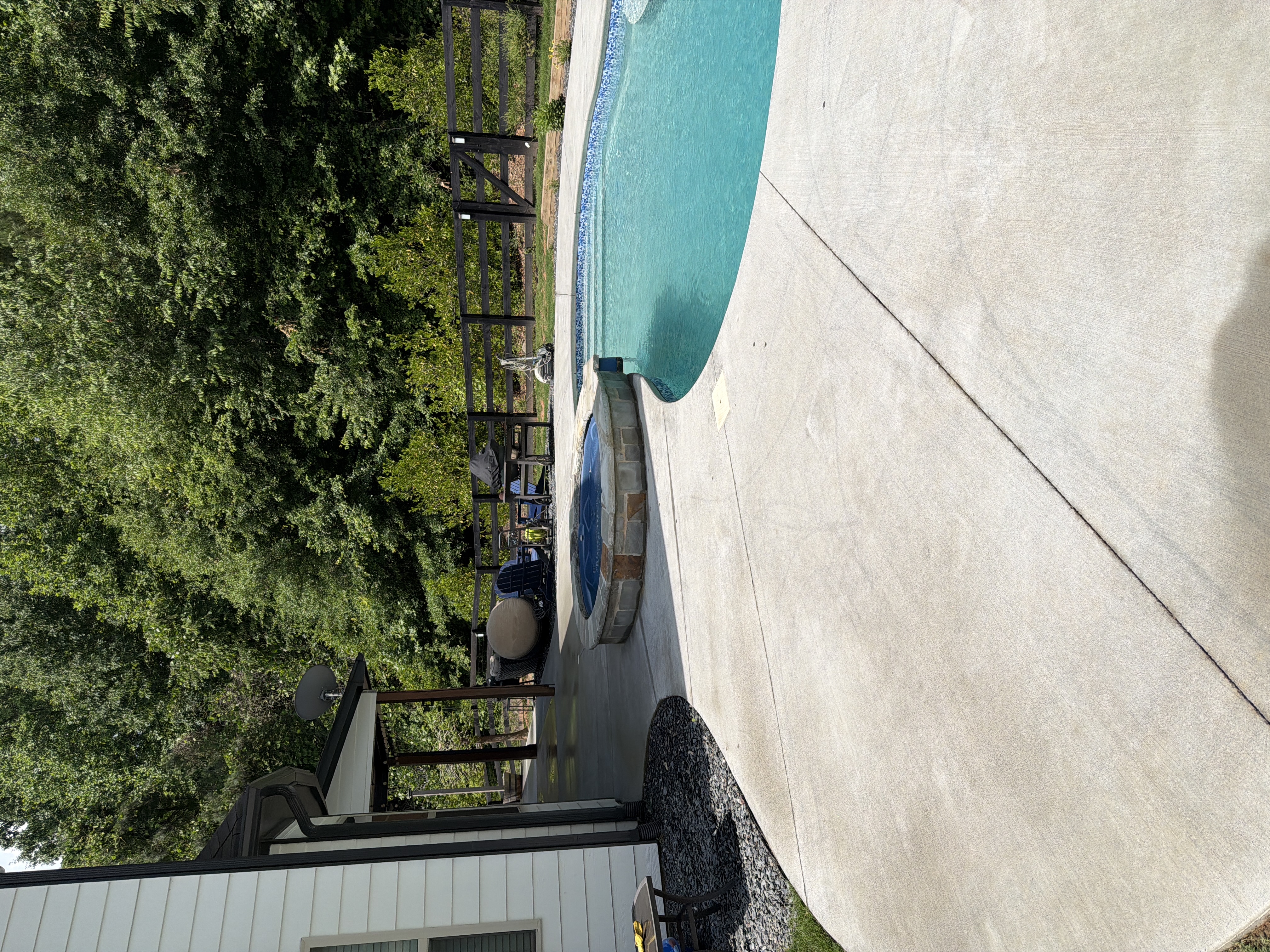 Clean concrete pool and spa deck after pressure washing in Canton, GA, wide view showing the full curved surround and backyard