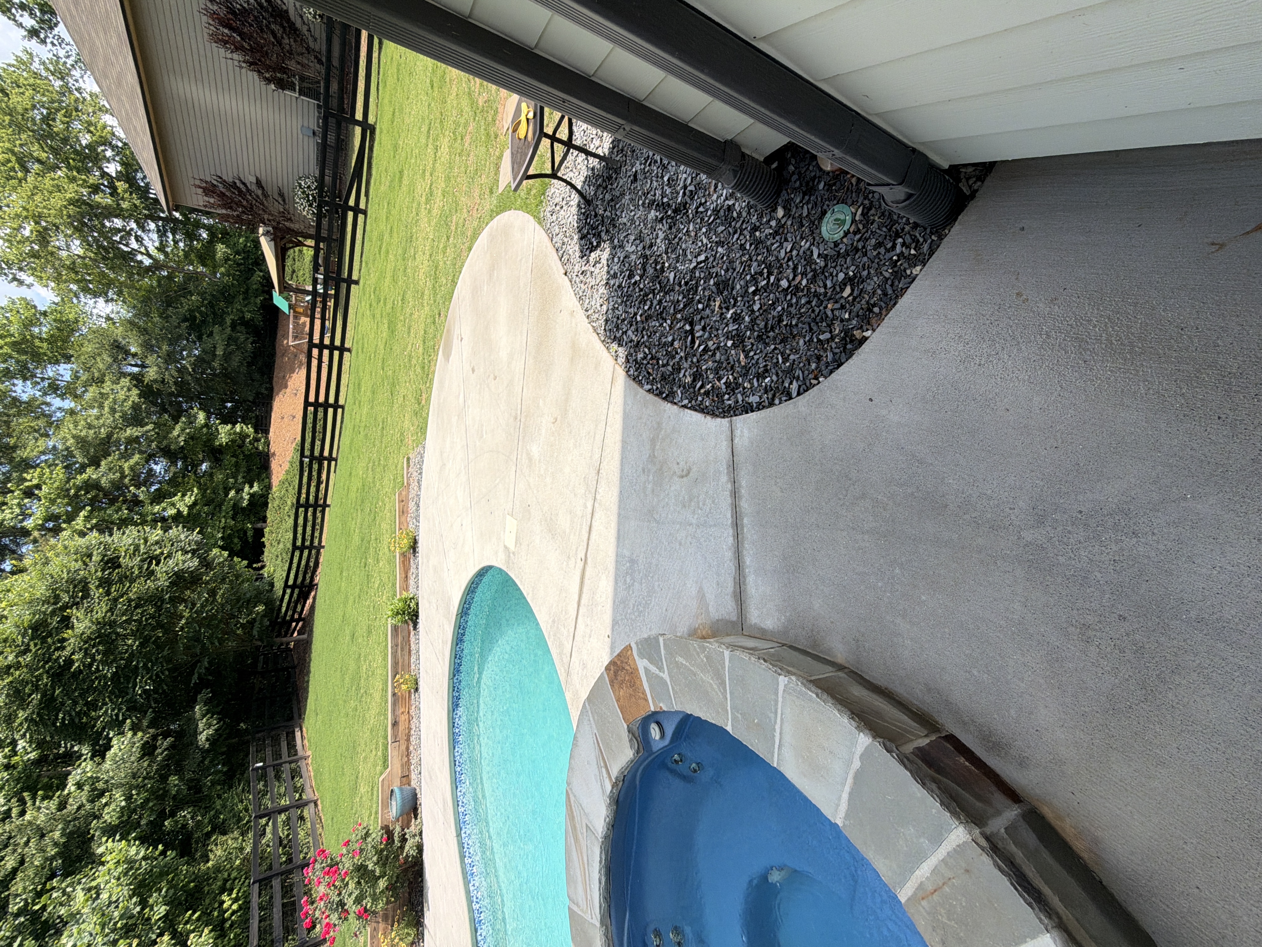 Clean concrete pool and spa deck after pressure washing in Canton, GA, with fenced green lawn and flowering shrubs visible