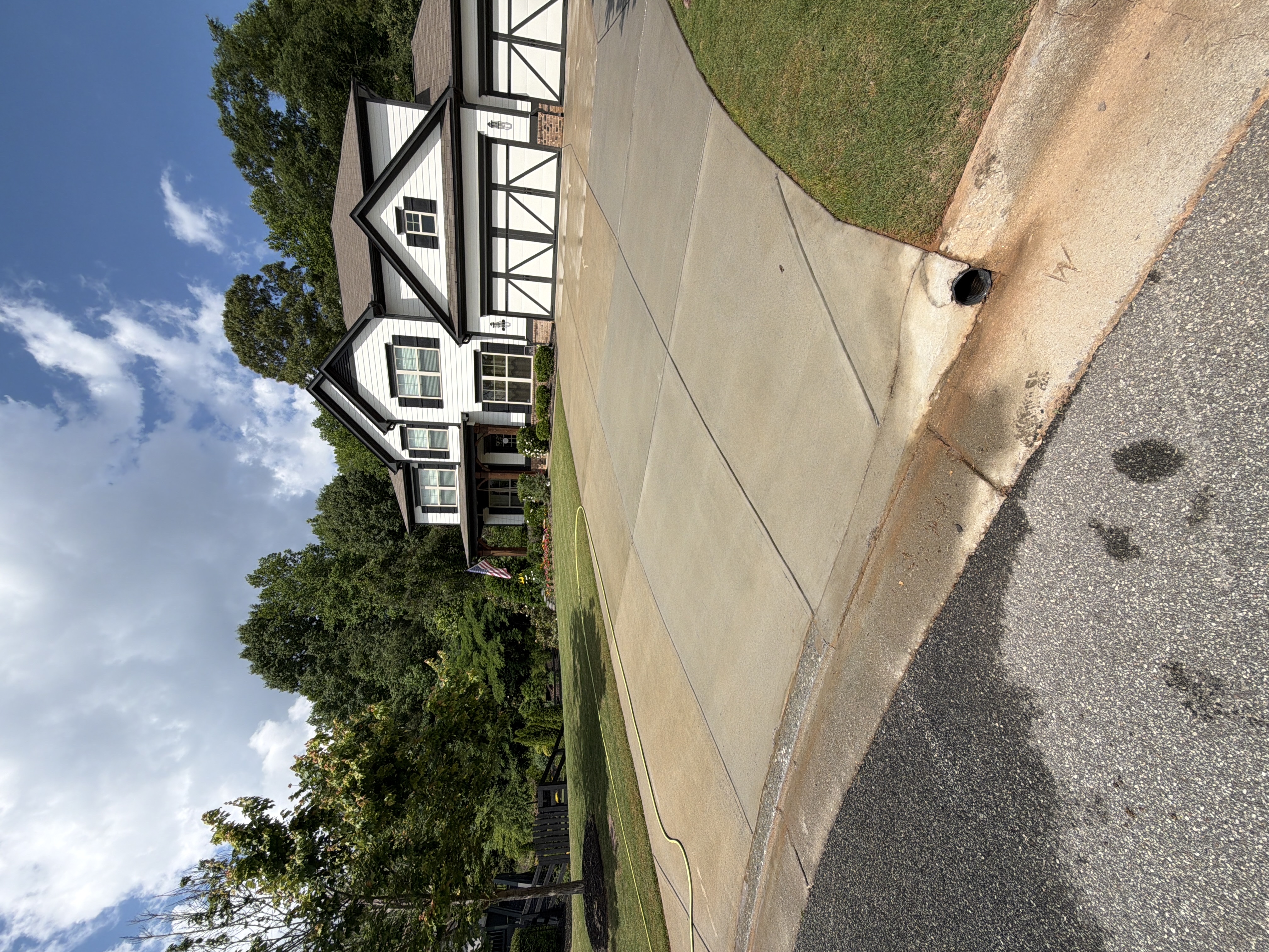 Wide shot of clean concrete driveway after pressure washing in Canton, GA, with three-car garage white farmhouse and blue sky backdrop