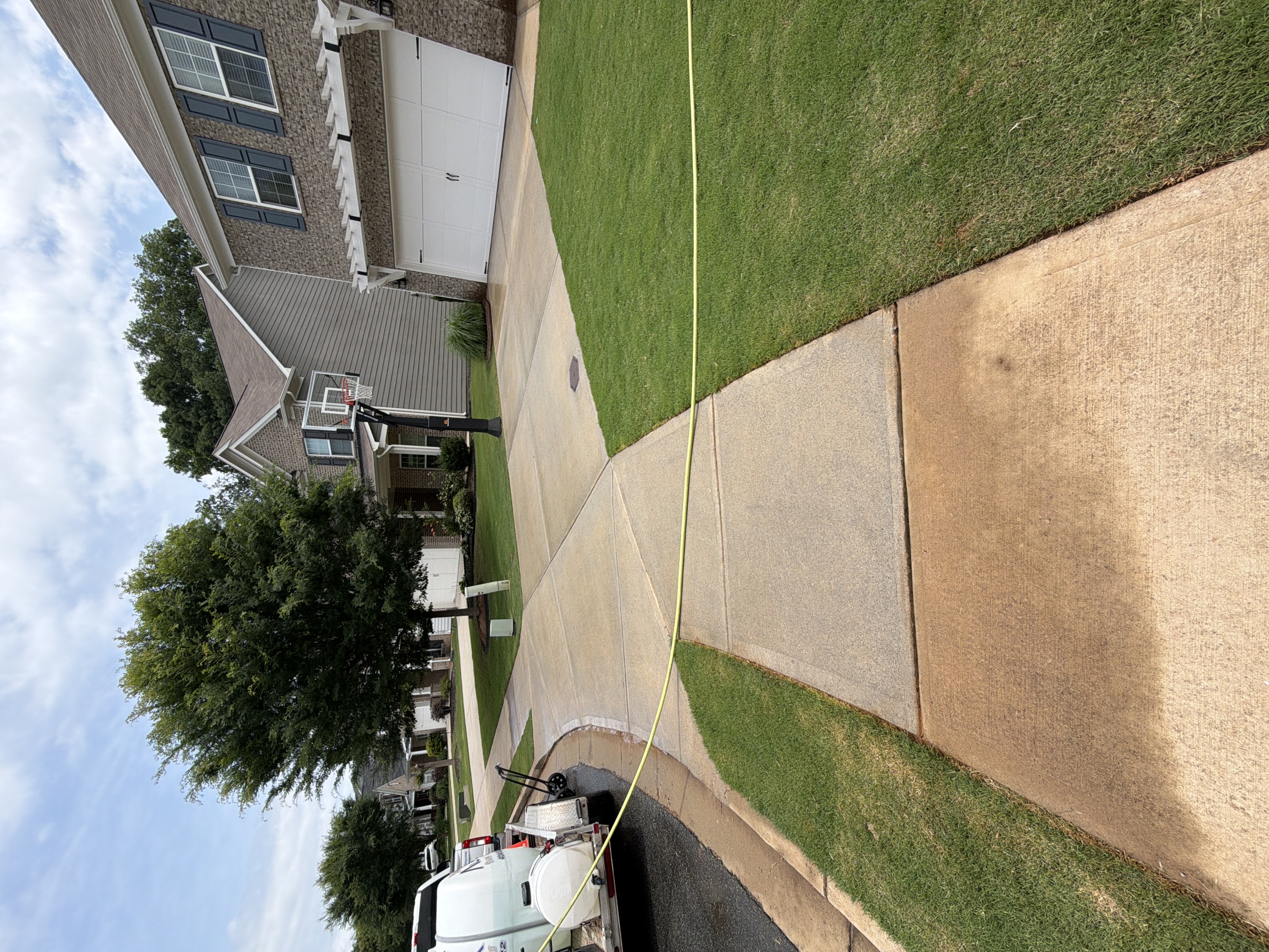 Concrete driveway and walkway cleaned by pressure washing in Canton, GA, service truck departing at left