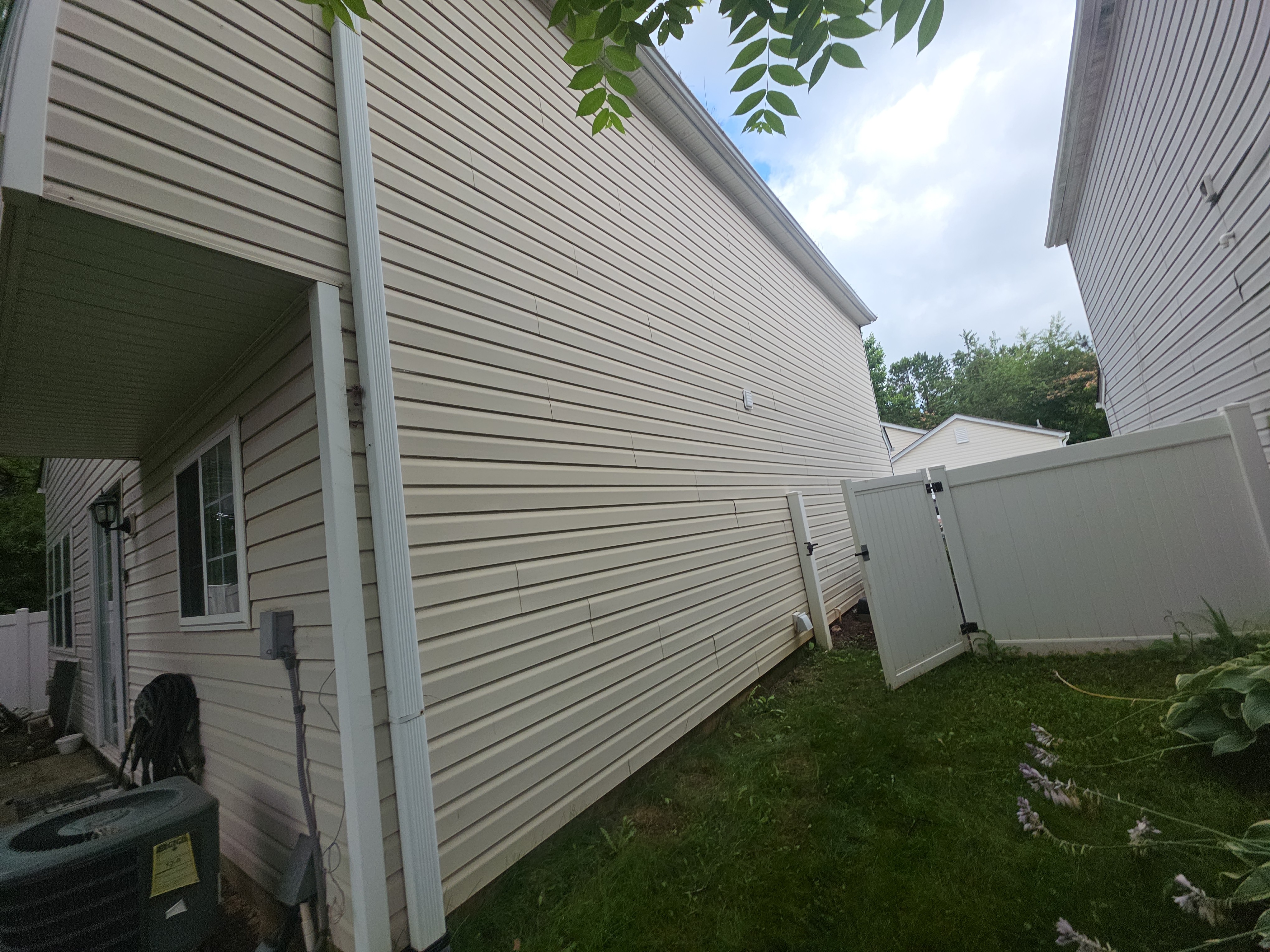 Side view of vinyl siding on a two-story home with a white vinyl fence gate visible at a house washing job in Woodstock, GA.