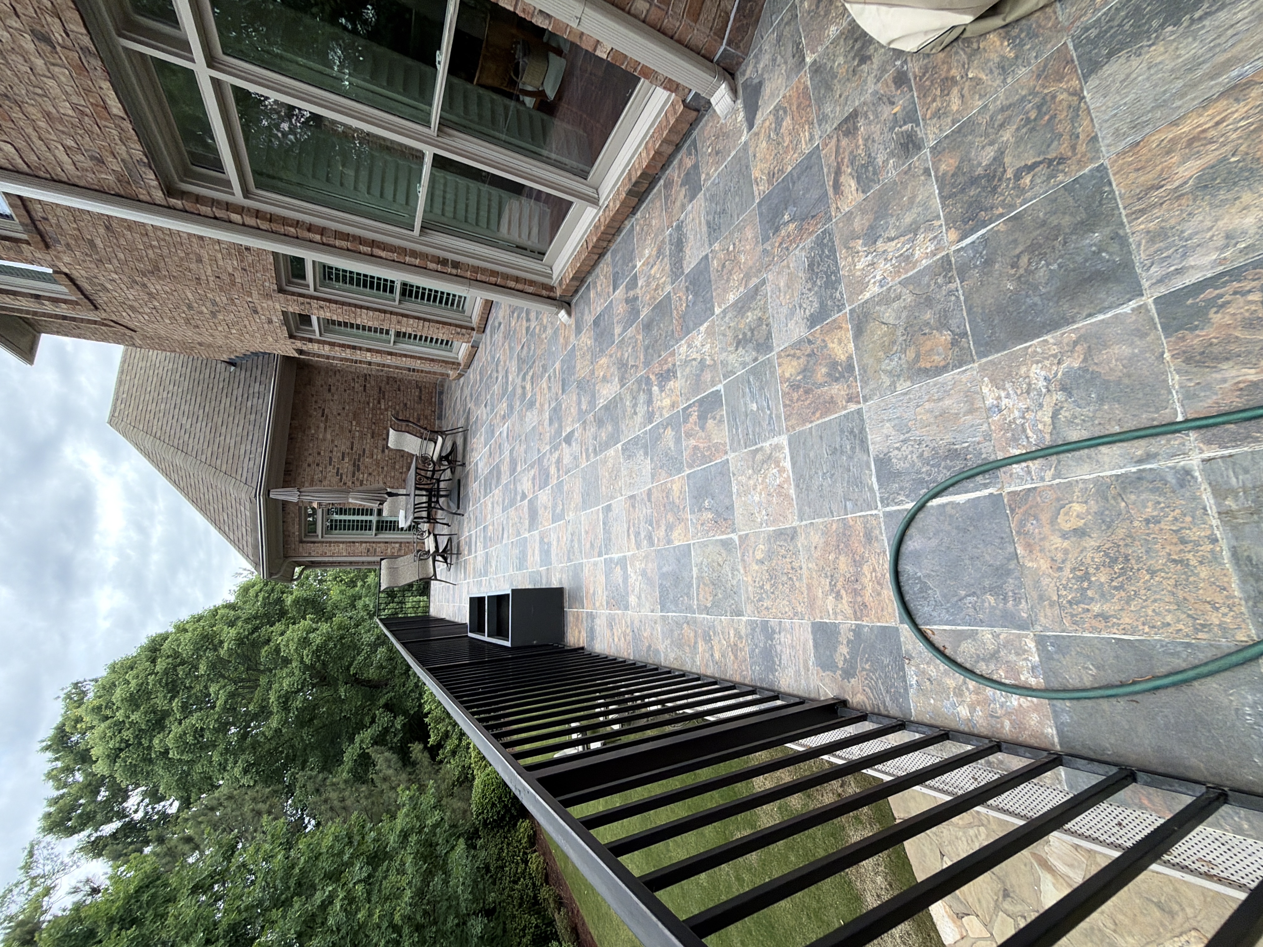 Wide view of a tile-paved upper deck with iron railing and garden hose coiled in the foreground at a Duluth, GA home.