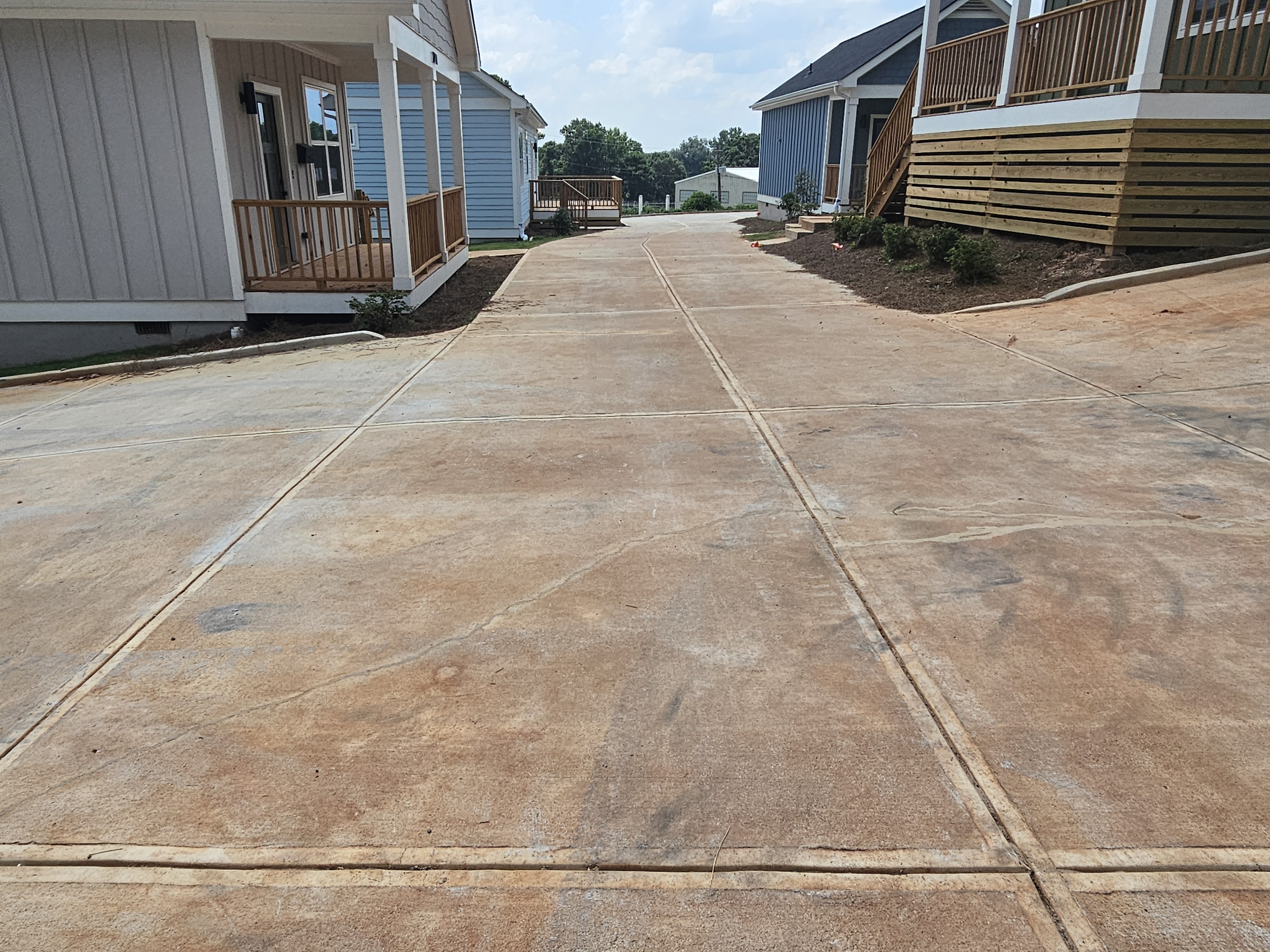 Wide concrete driveway between new construction homes at a pressure washing job in Atlanta, GA, showing rust and soil staining.