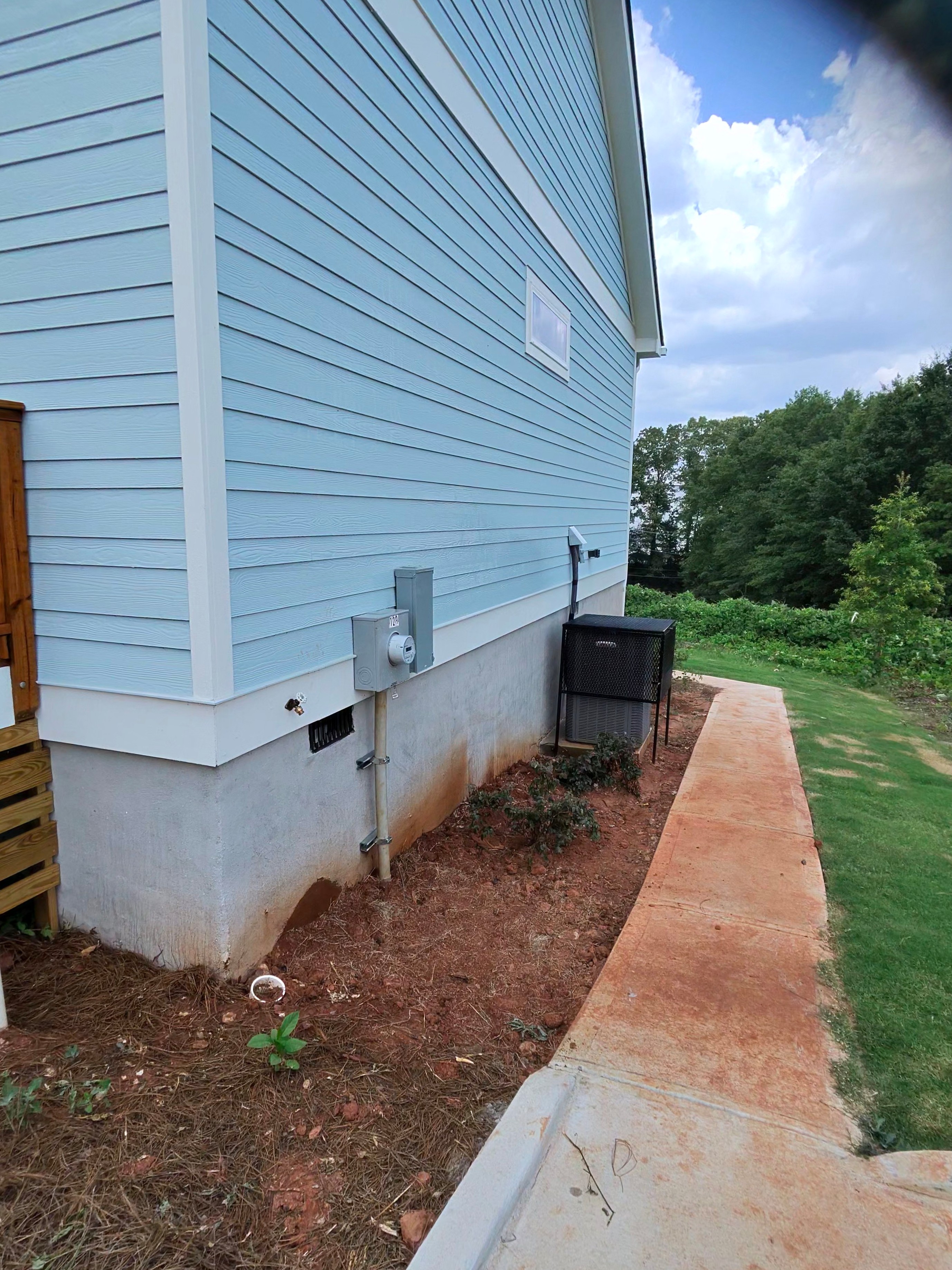Side of a new construction home showing light blue vinyl siding and concrete block foundation with rust staining at an Atlanta, GA pressure washing job.