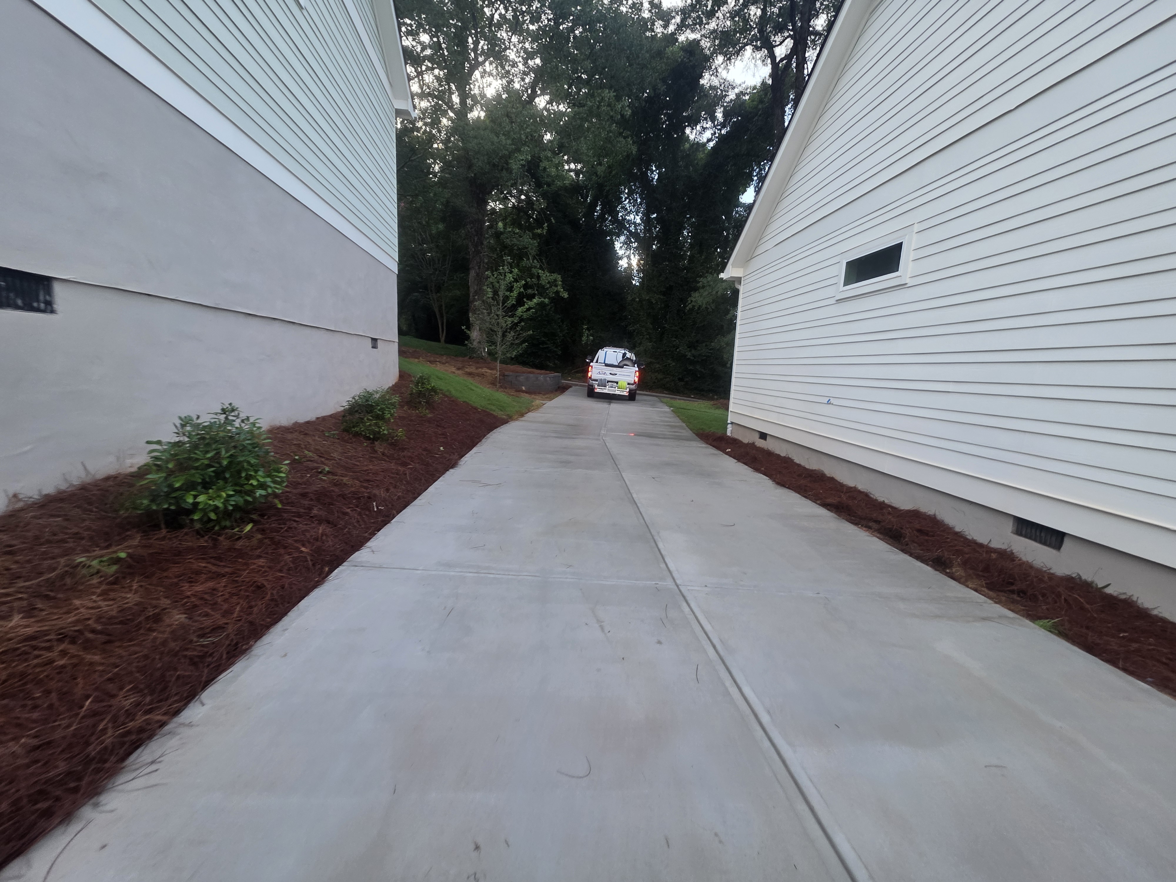 Concrete driveway between new construction homes after pressure washing in Atlanta, GA, with pressure washing truck visible in background.