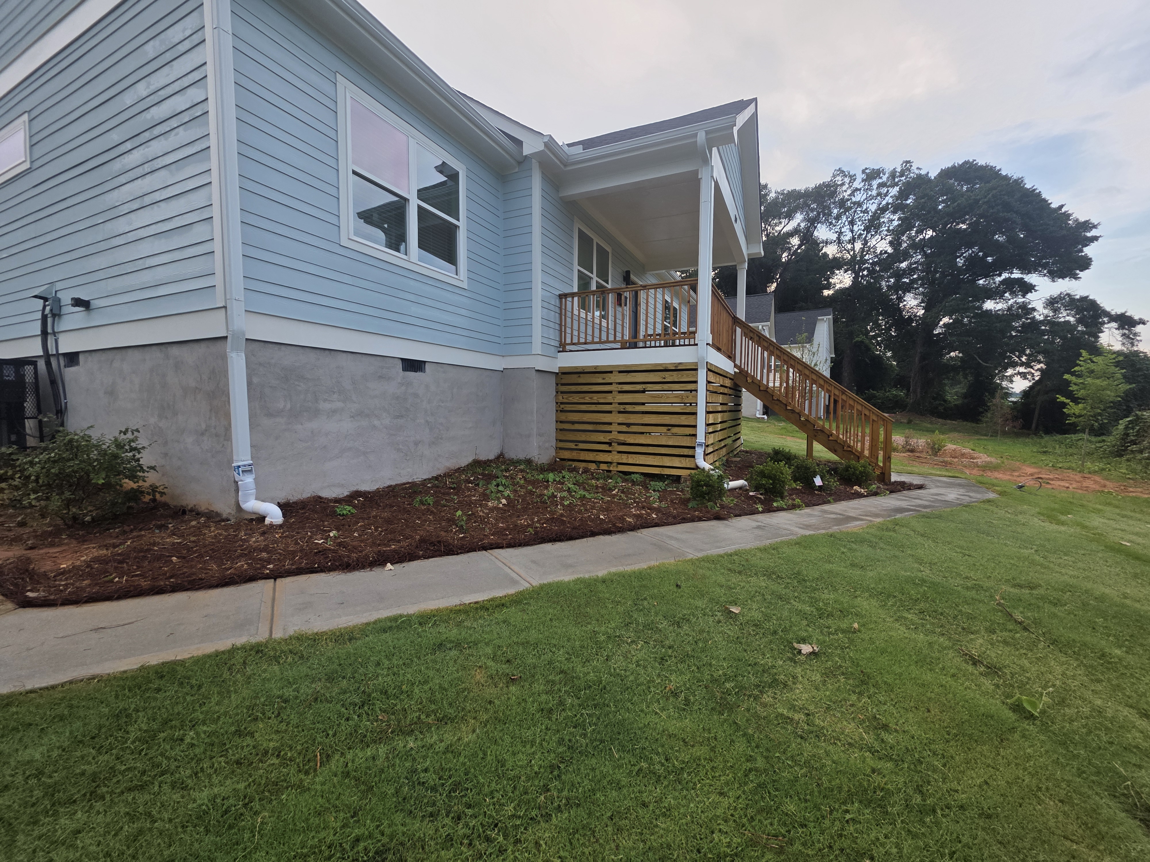 Side view of a new construction home with blue vinyl siding, concrete block foundation, wood deck, and concrete walkway in Atlanta, GA.