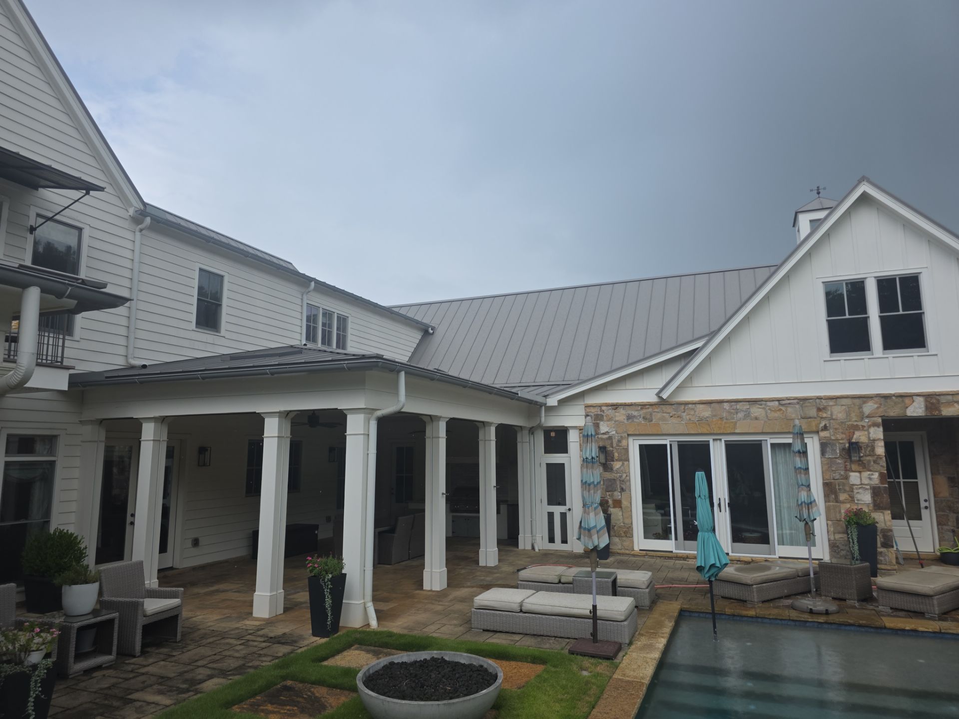 Rear exterior of a large white farmhouse with standing-seam metal roof and stone accents at a Milton, GA pressure washing job.