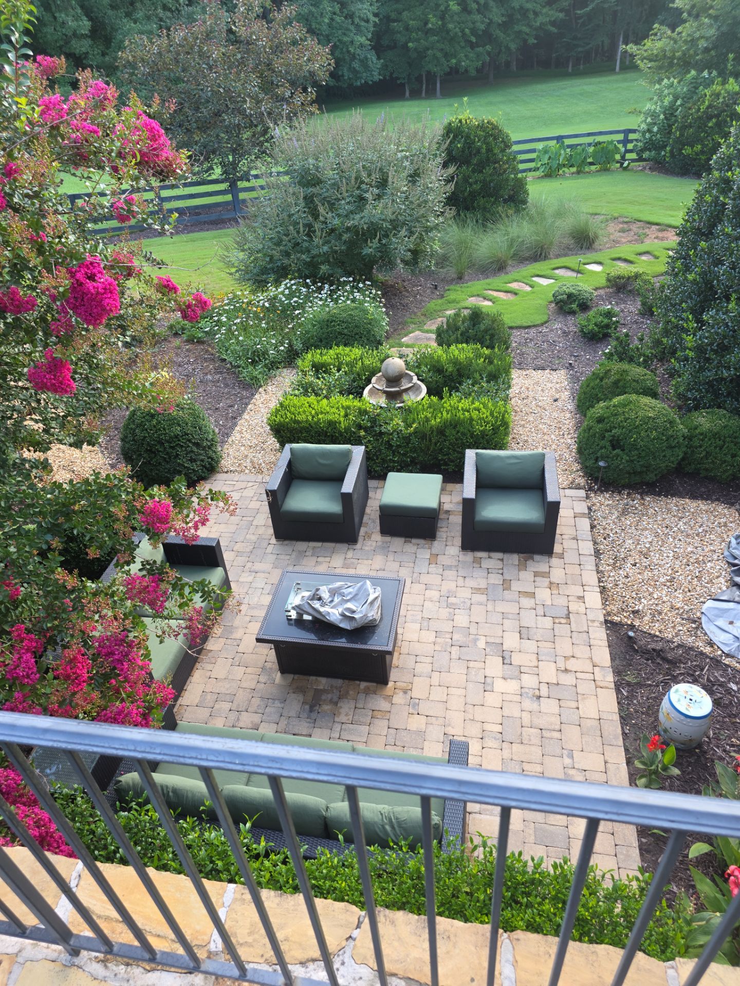 Aerial view of a brick-paver patio with outdoor furniture and a water fountain surrounded by manicured gardens in Milton, GA.