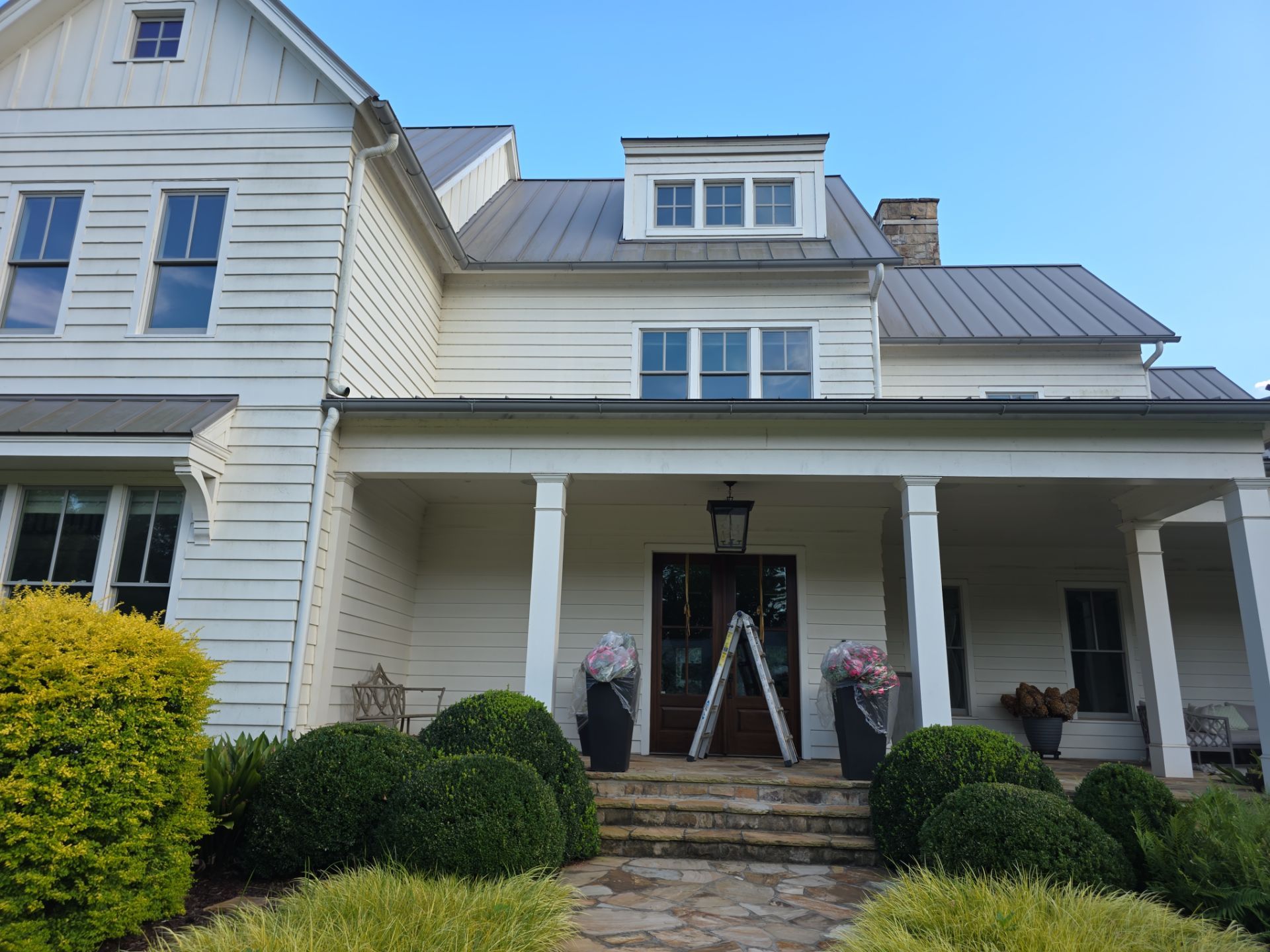 Front exterior of a white two-story farmhouse with a metal roof and covered porch during a house washing job in Milton, GA.