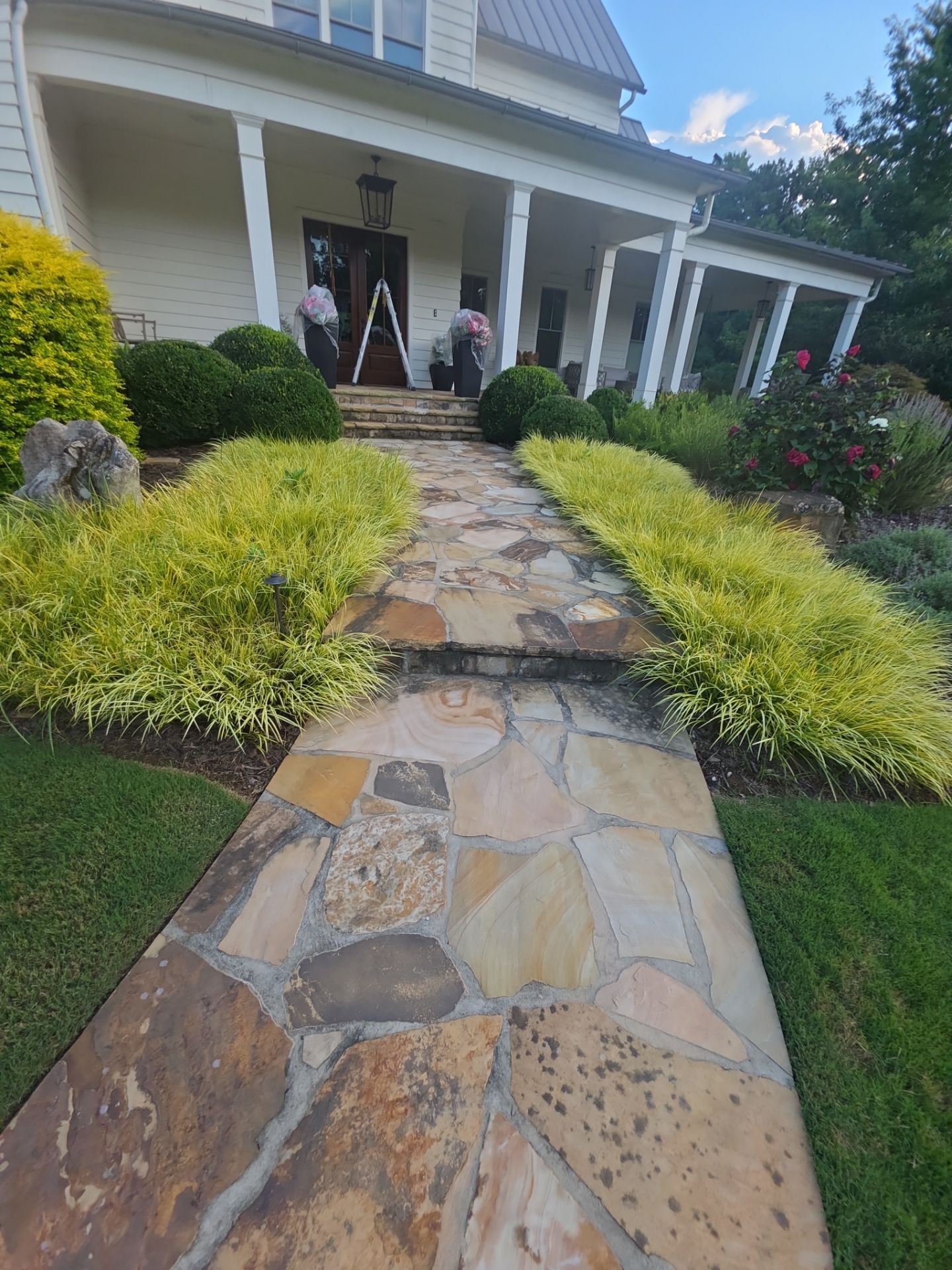 Flagstone front walkway lined with ornamental grasses leading to the porch of a white farmhouse in Milton, GA.