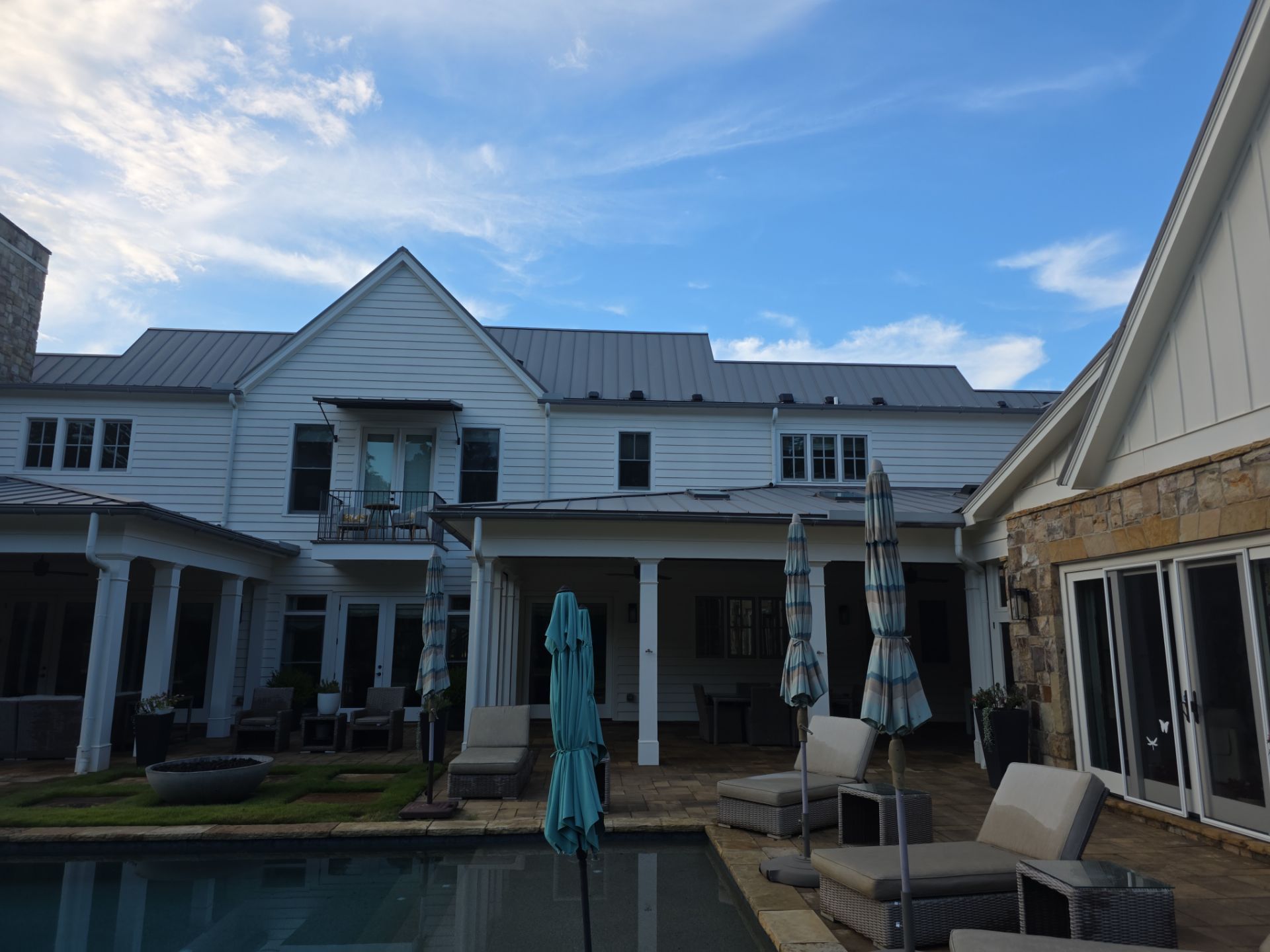 Rear view of a white farmhouse with a backyard pool, stone patio, and covered porch at a Milton, GA pressure washing job.