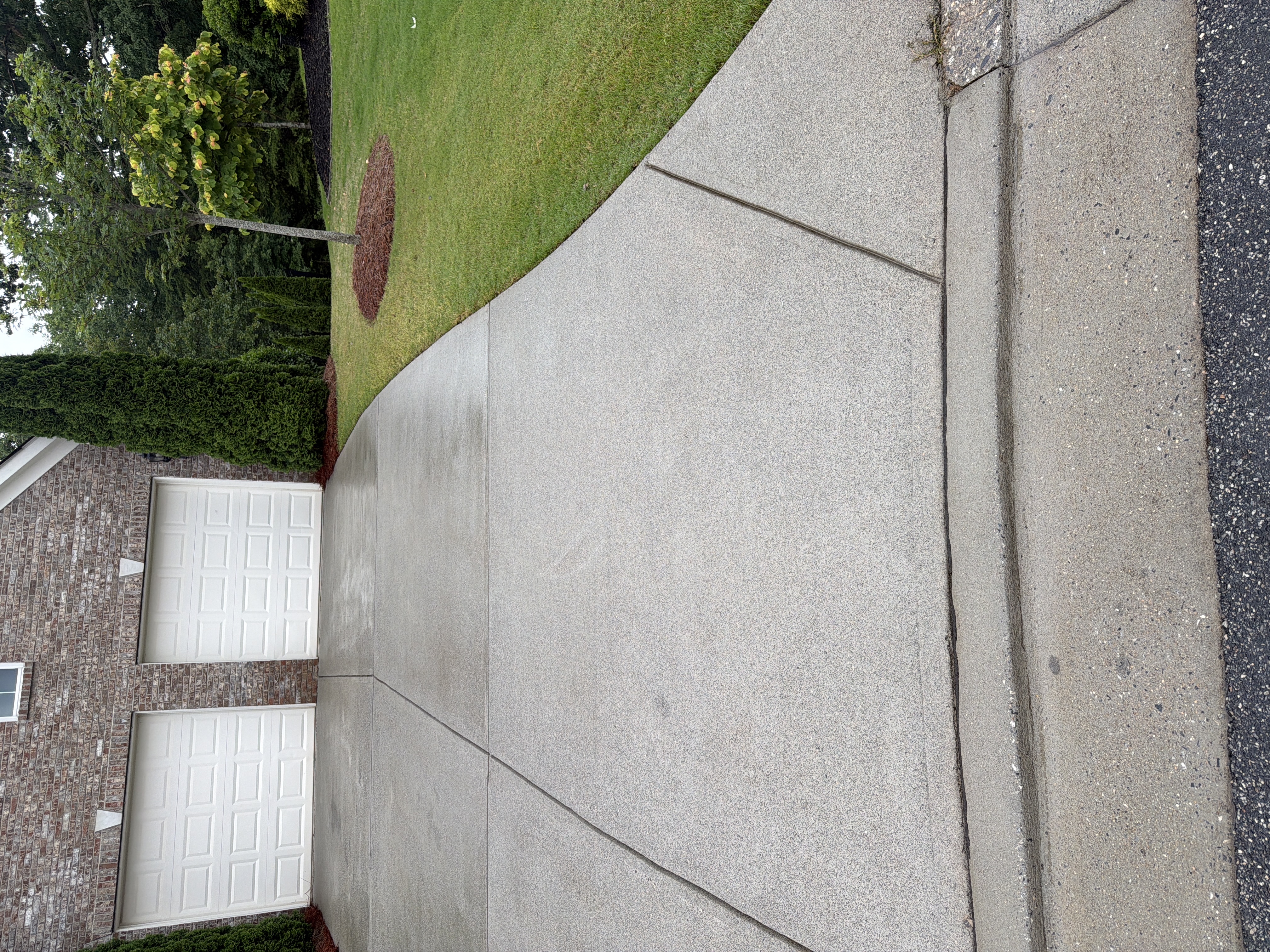 Wide concrete driveway pressure-washed clean in Cumming, GA, brick home with two-car garage and green landscaping