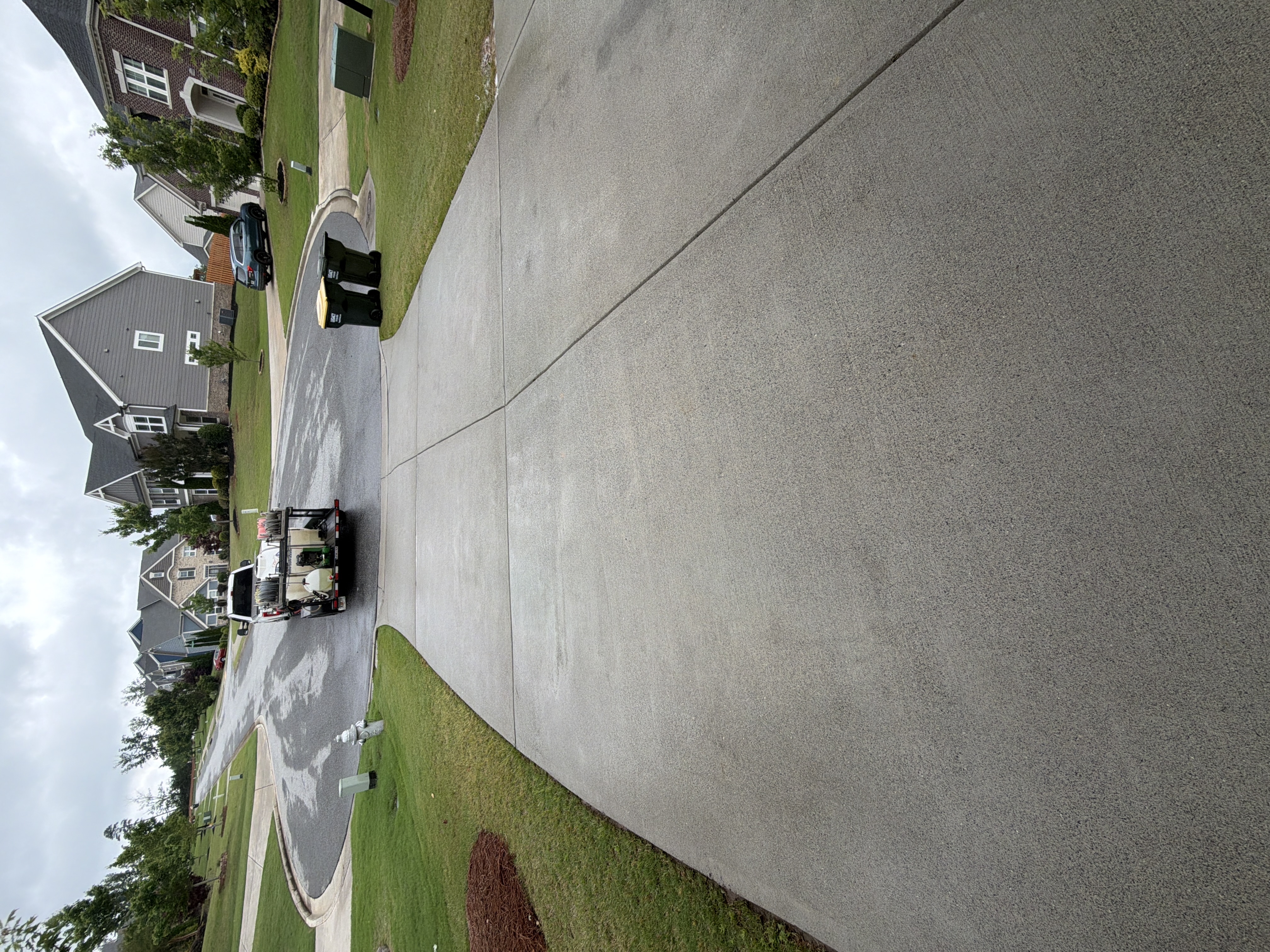 Clean concrete driveway after pressure washing in Cumming, GA, pressure-washing truck visible departing in background