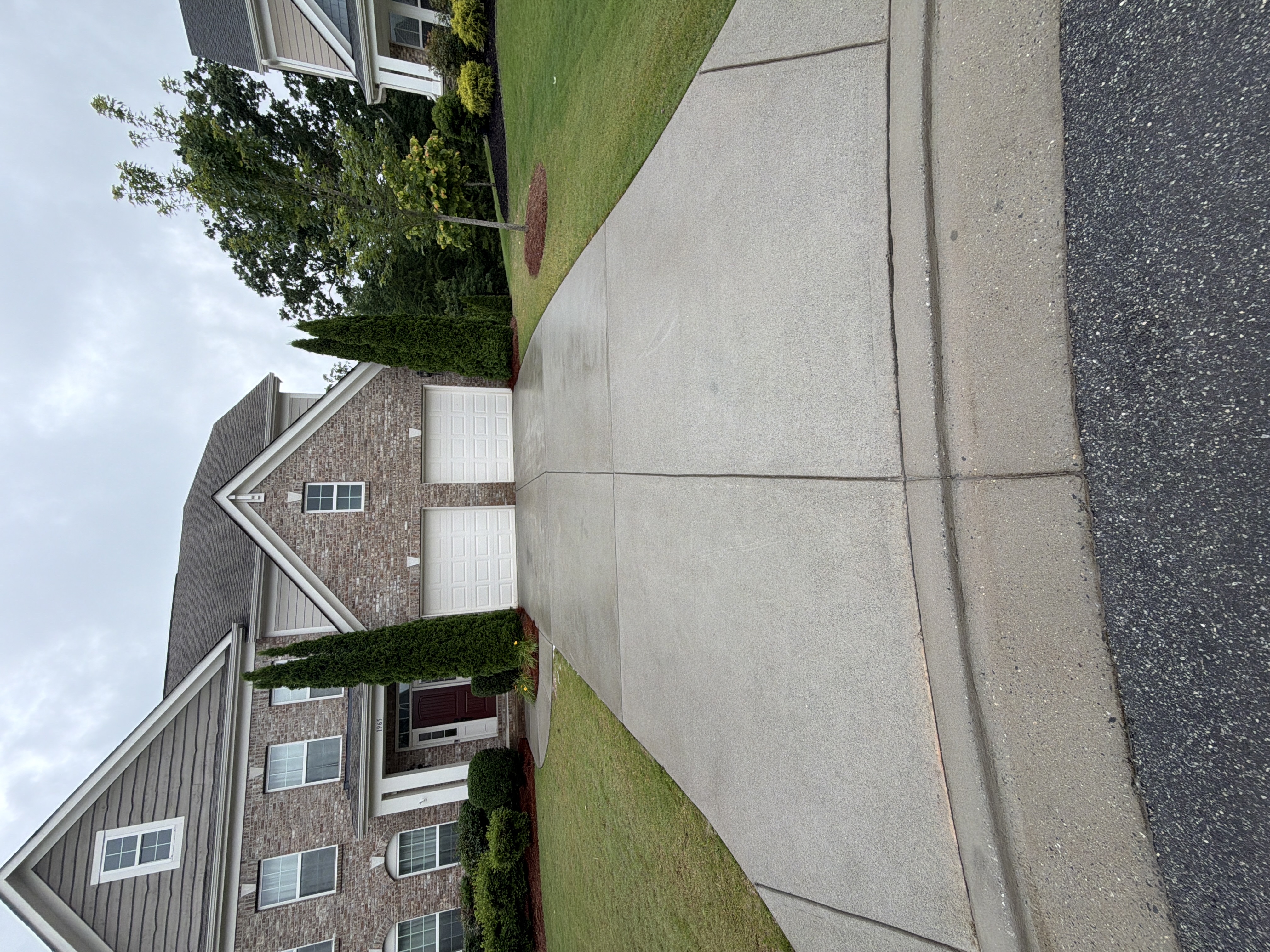 Wide concrete driveway pressure-washed clean in Cumming, GA, full-width view of two-story brick and siding home