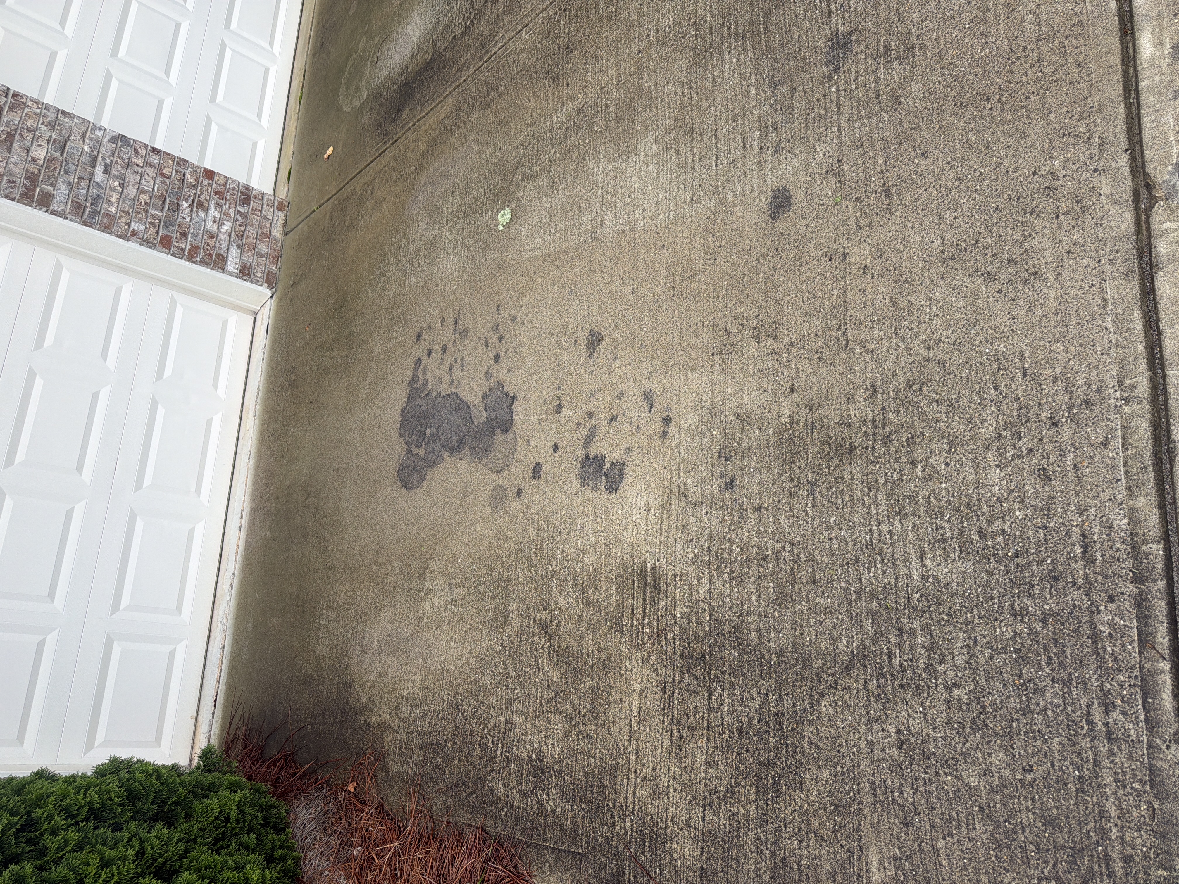 Concrete driveway with prominent oil stains near garage before pressure washing service in Cumming, GA